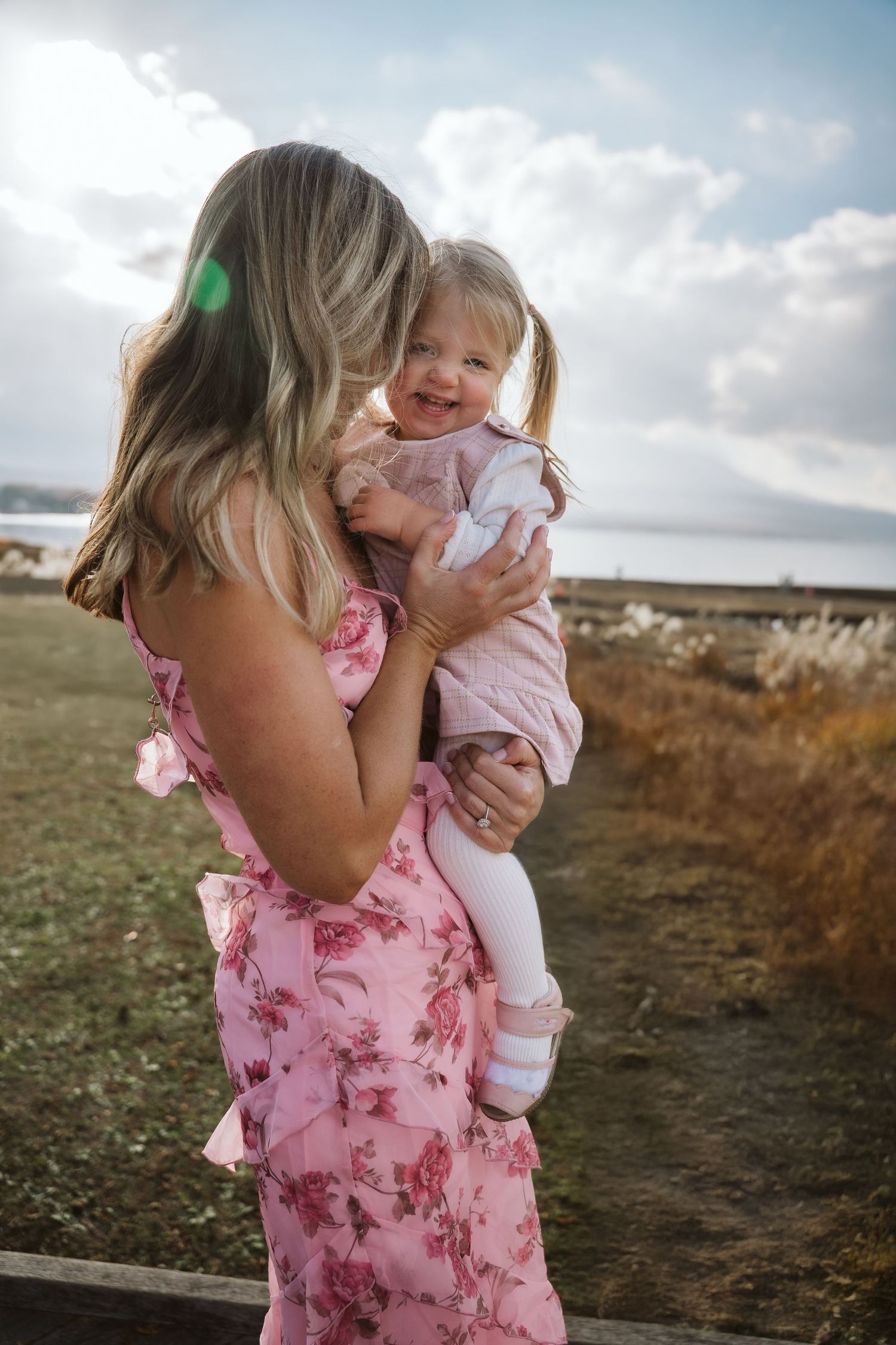 A touching moment captured outdoors as a mother in a pink floral dress holds her smiling young child.