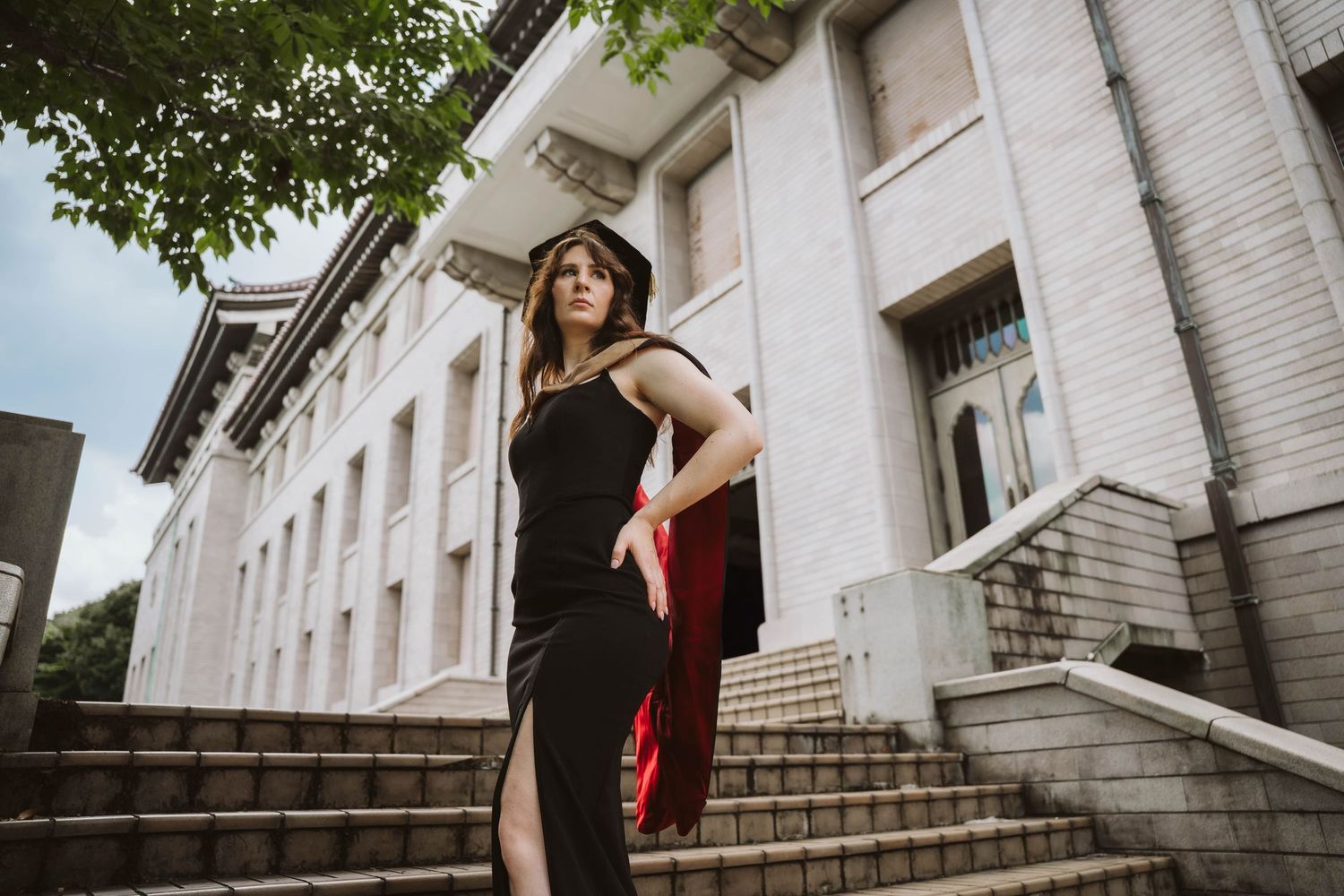 A person in a red dress poses elegantly on white stone steps of a classic architectural building.