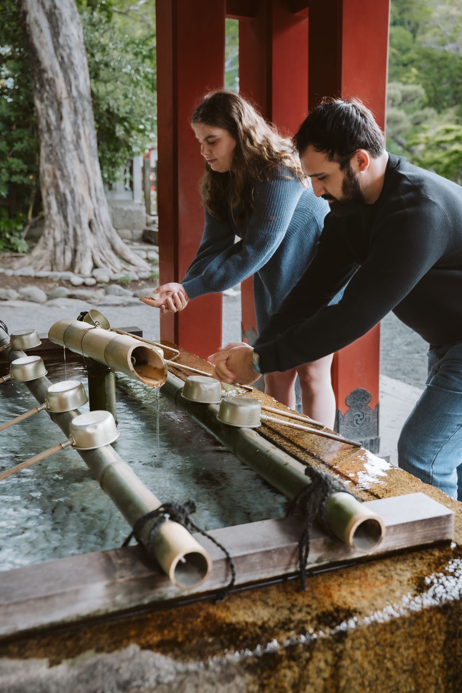 People performing ritual purification at a traditional Japanese chozuya water basin in a temple.