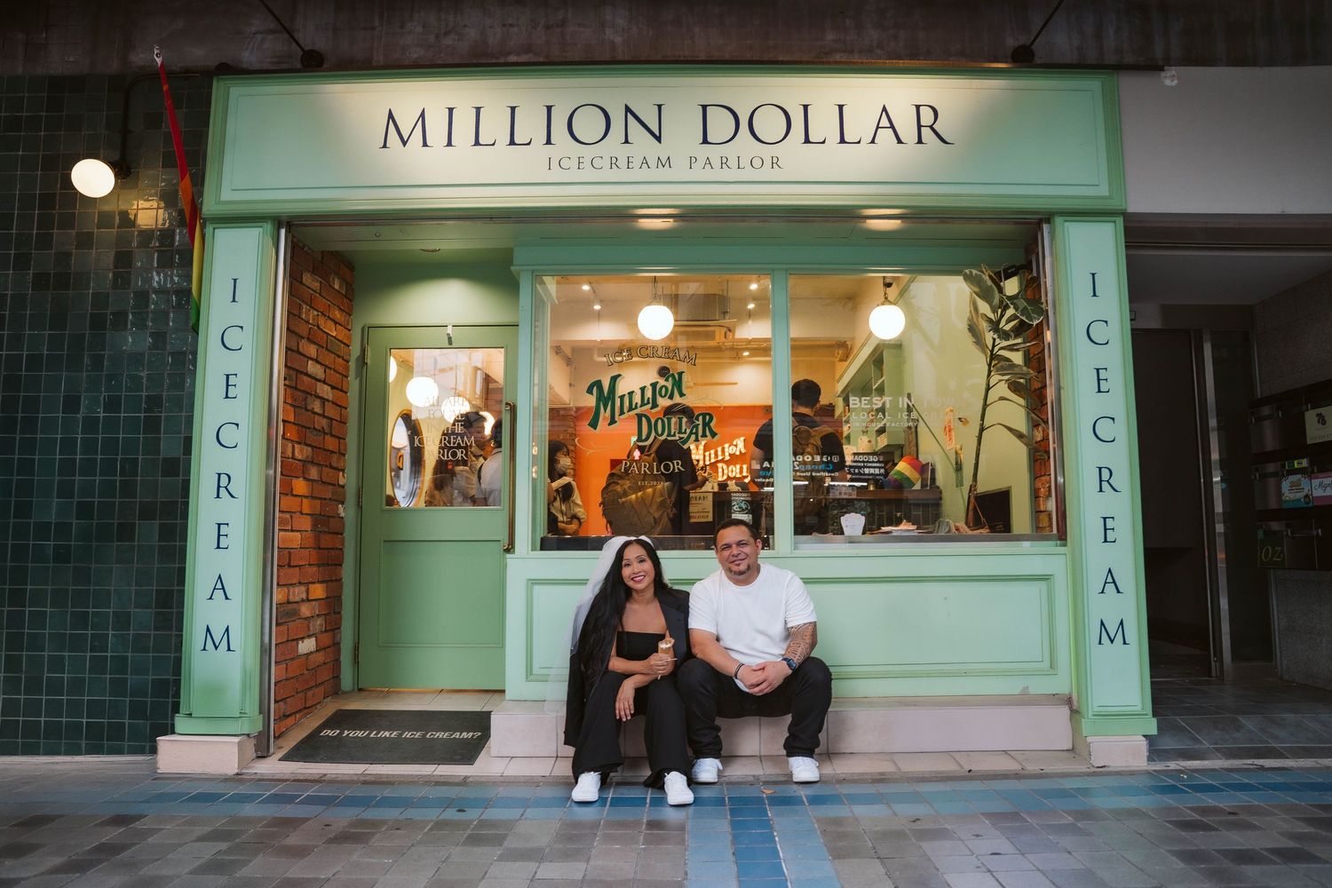 Two people sitting on steps in front of a storefront with 'Million Dollar' signage at night.