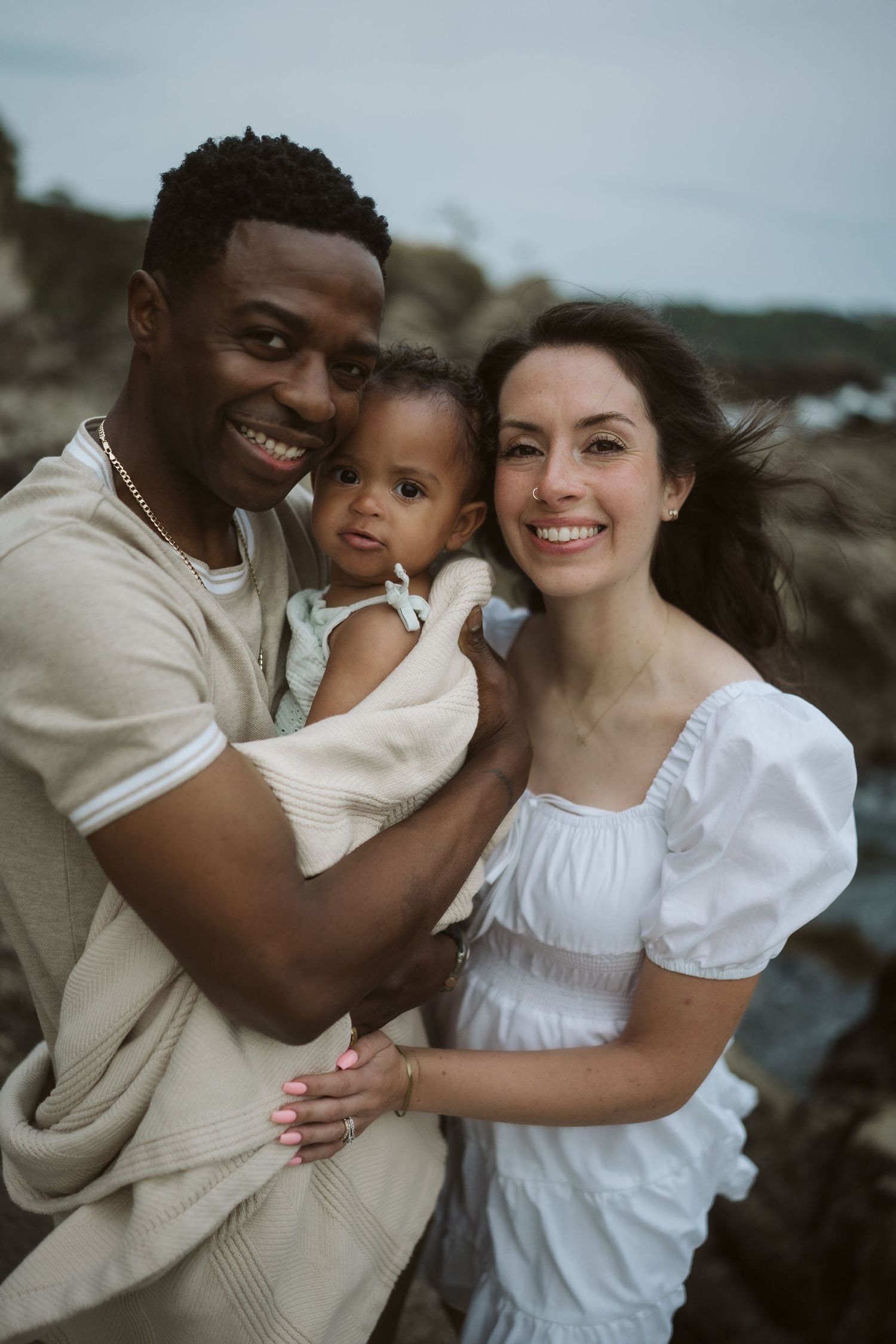 An intimate family portrait session captures tender moments against a moody coastal backdrop.