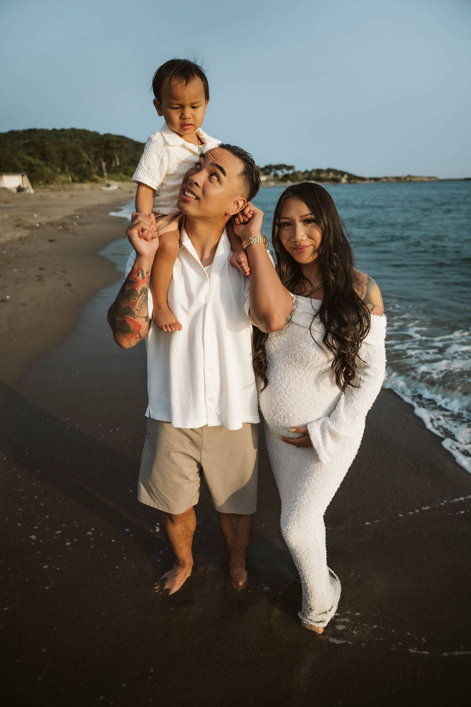 A family enjoys a tender moment together on a scenic beach at sunset with waves lapping at the shore.