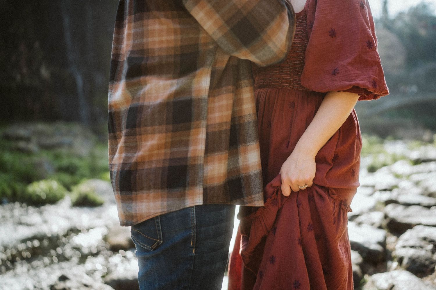 Couple in plaid and burgundy outfits holding hands while walking through a snowy winter landscape.