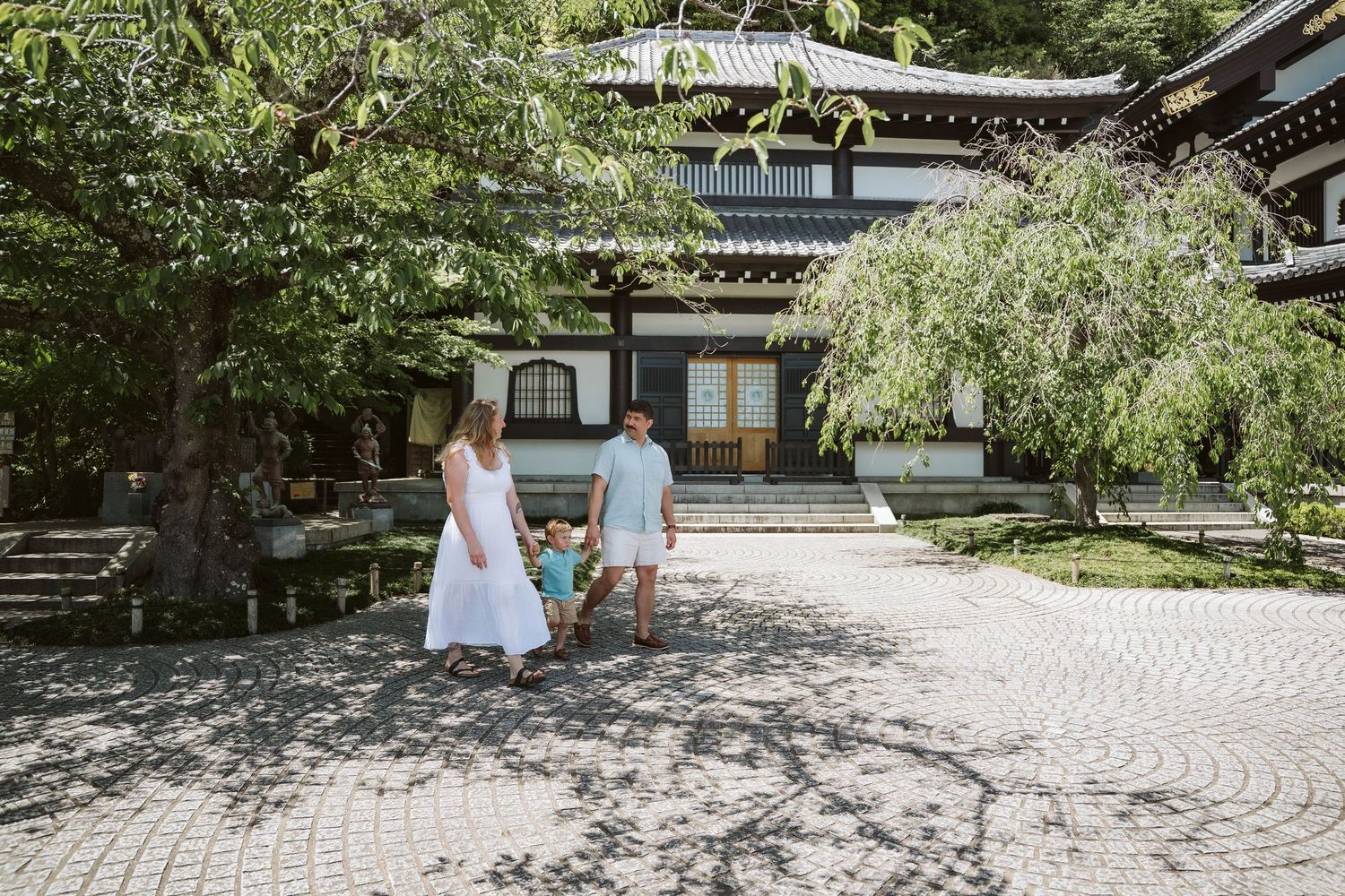 A serene Japanese garden walkway with stone paths and lush greenery surrounds a traditional wooden building.