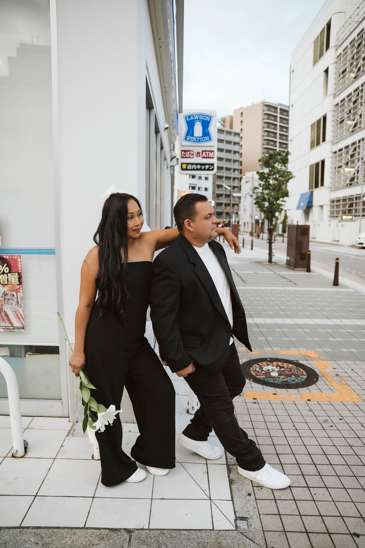 Couple in black and white outfits sitting and posing on urban sidewalk in progressive sequence of photos.