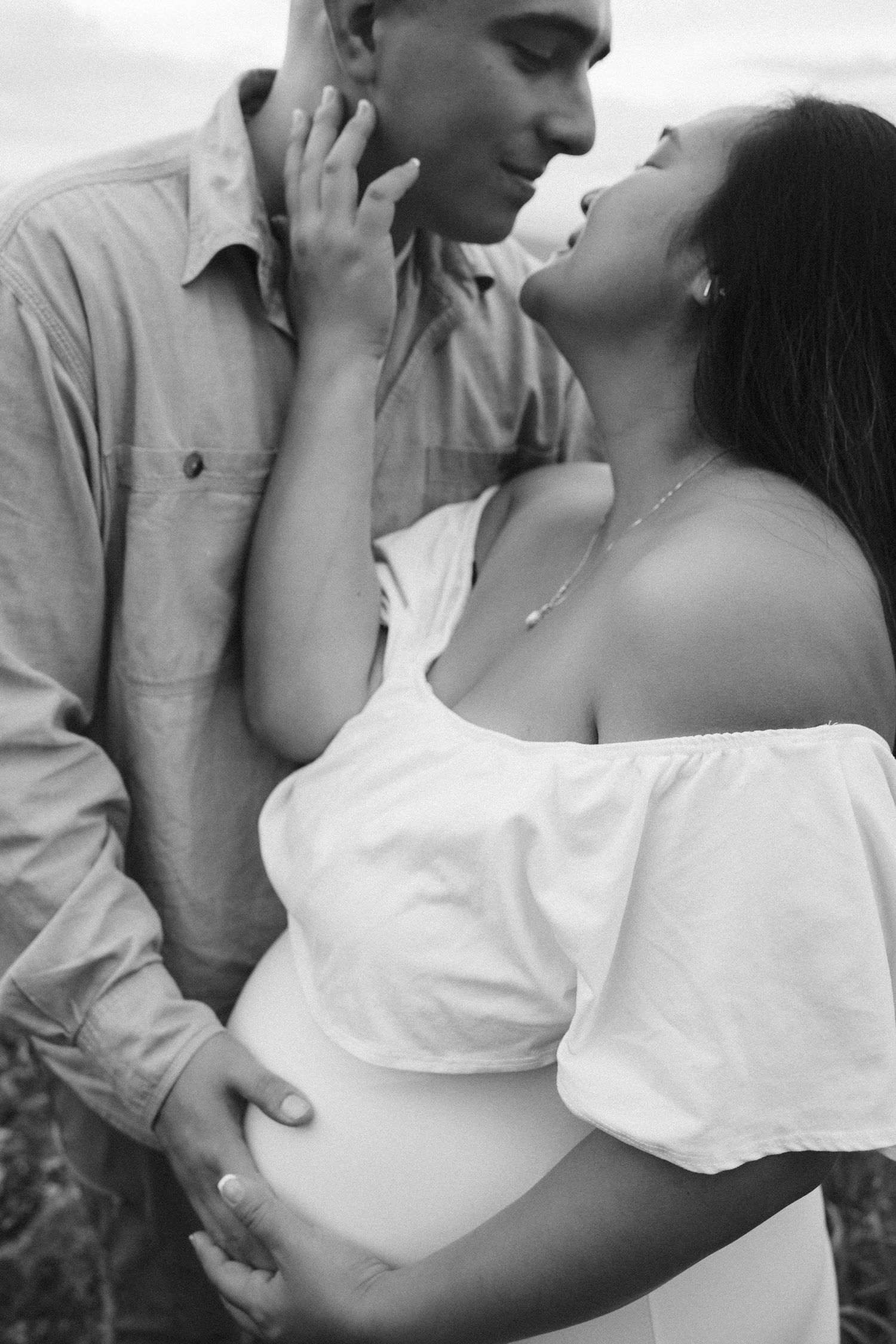 A romantic black and white portrait of an intimate couple embracing, with her wearing a flowy white off-shoulder top.