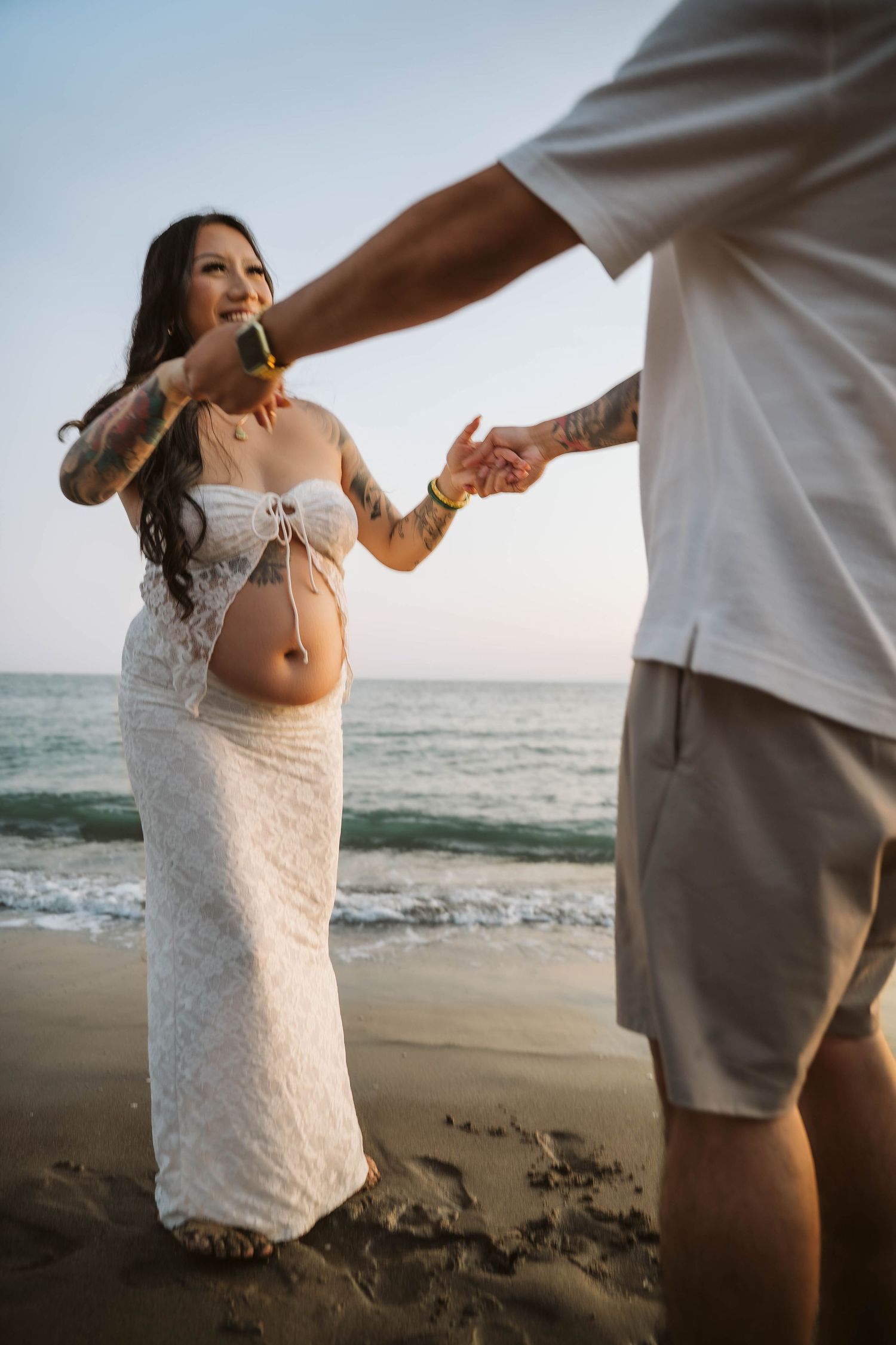 Couple dancing together on sandy beach at sunset during pregnancy photoshoot.