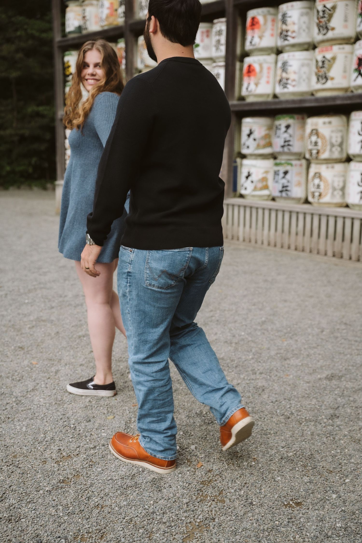 Two people standing near sake barrels at a shrine, with focus on their legs and orange shoes.