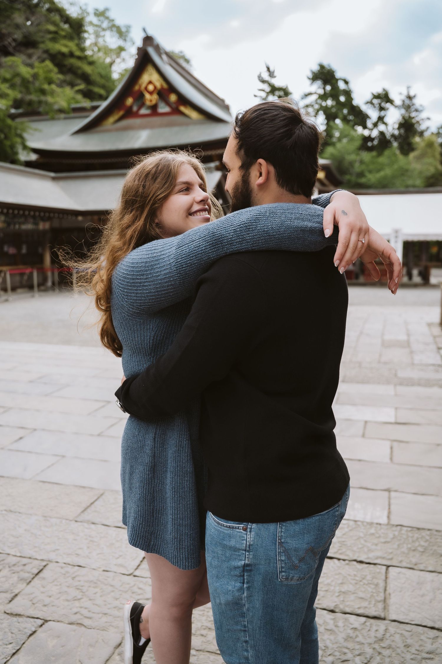 Romantic couple embraces on stone pathway near traditional Japanese temple architecture.