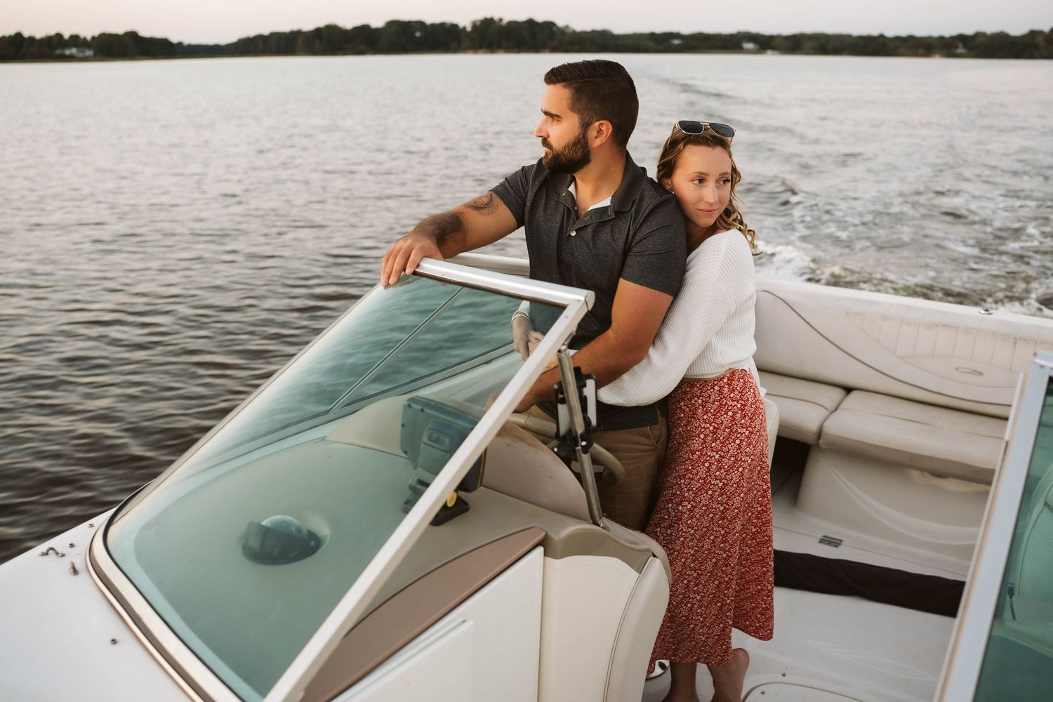 A couple enjoys a romantic moment on a boat while cruising across a serene lake at sunset.