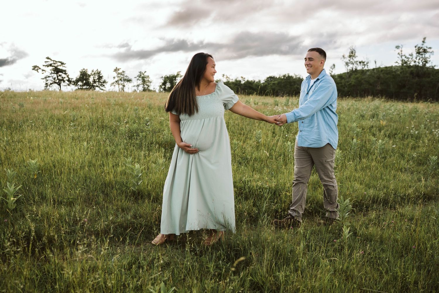 Couple dancing together in a grassy meadow at sunset, wearing light colored clothing.