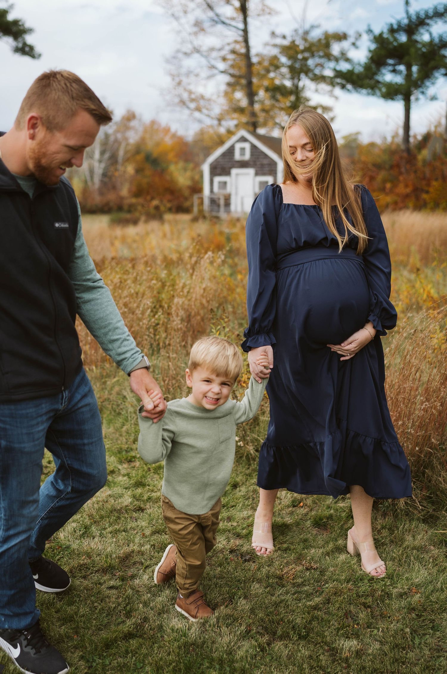 A family enjoys an autumn day together in a field with a small cottage in the background.