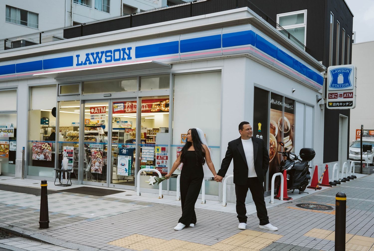 A couple walks hand in hand past a Lawson convenience store in Japan at dusk.