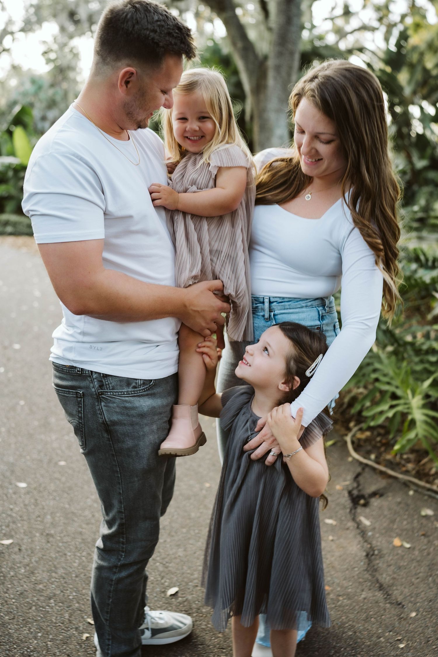 A happy family shares a joyful moment together outdoors, dressed casually in white tops and denim on a garden path.