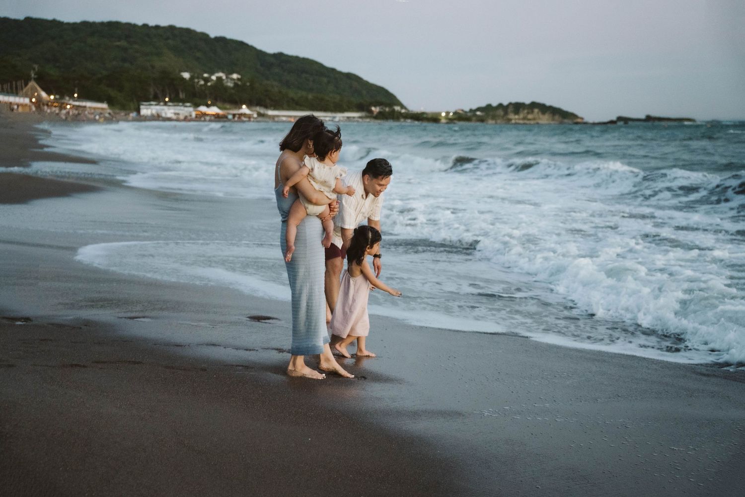Family walking and playing along a scenic coastal beach with waves crashing against the shore.