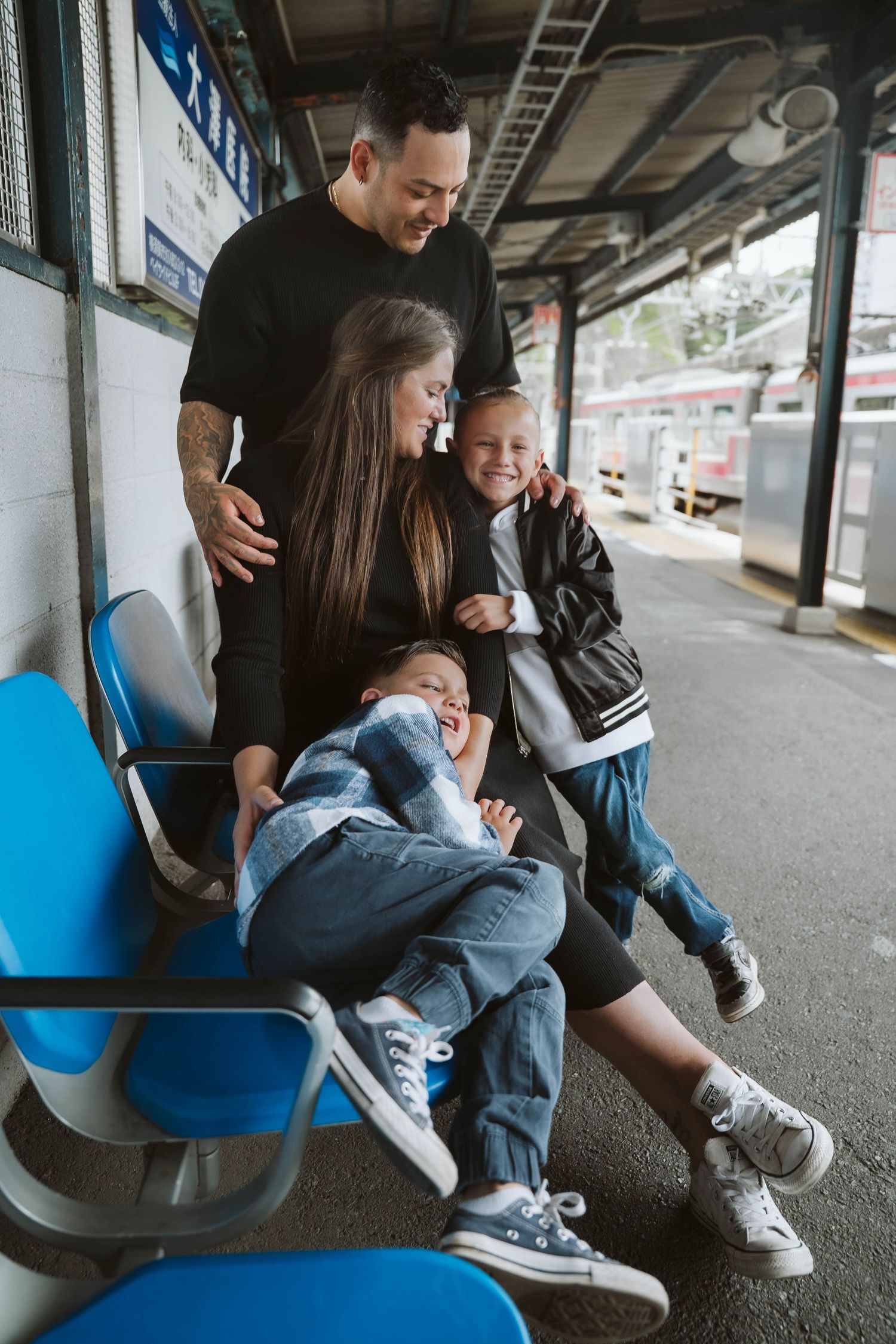 Family sharing a tender moment while seated on blue benches at a transit station.