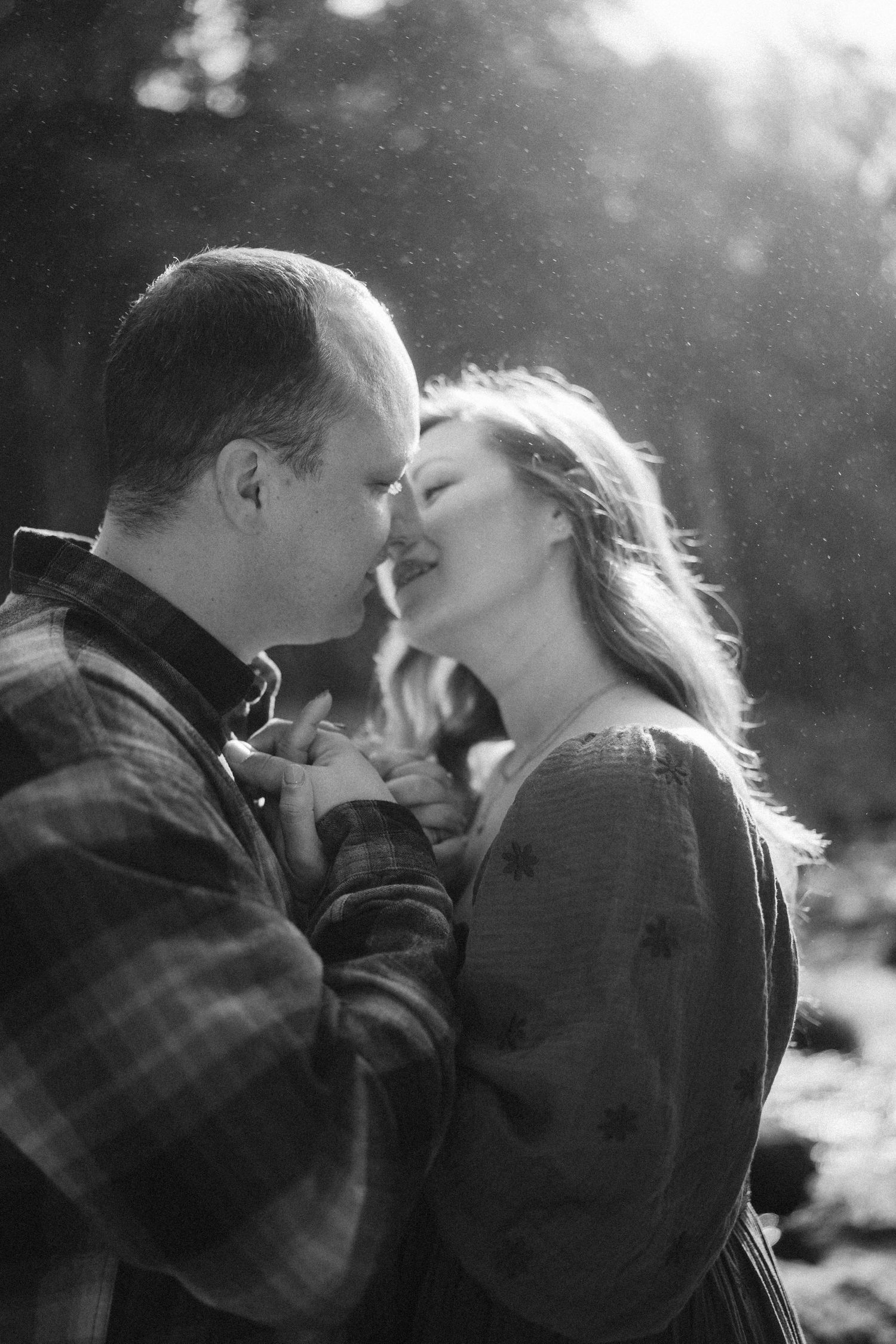 A romantic black and white portrait captures an intimate moment between a couple in natural lighting.