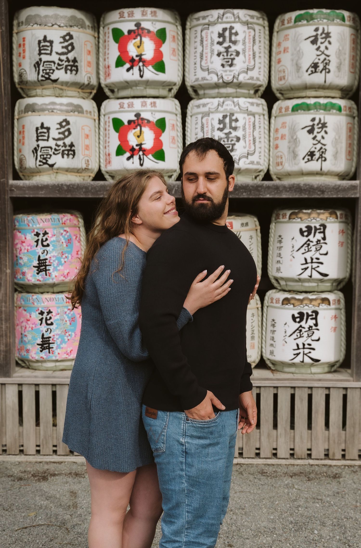 Japanese sake barrels with traditional calligraphy displayed on wooden shelves at a shrine.