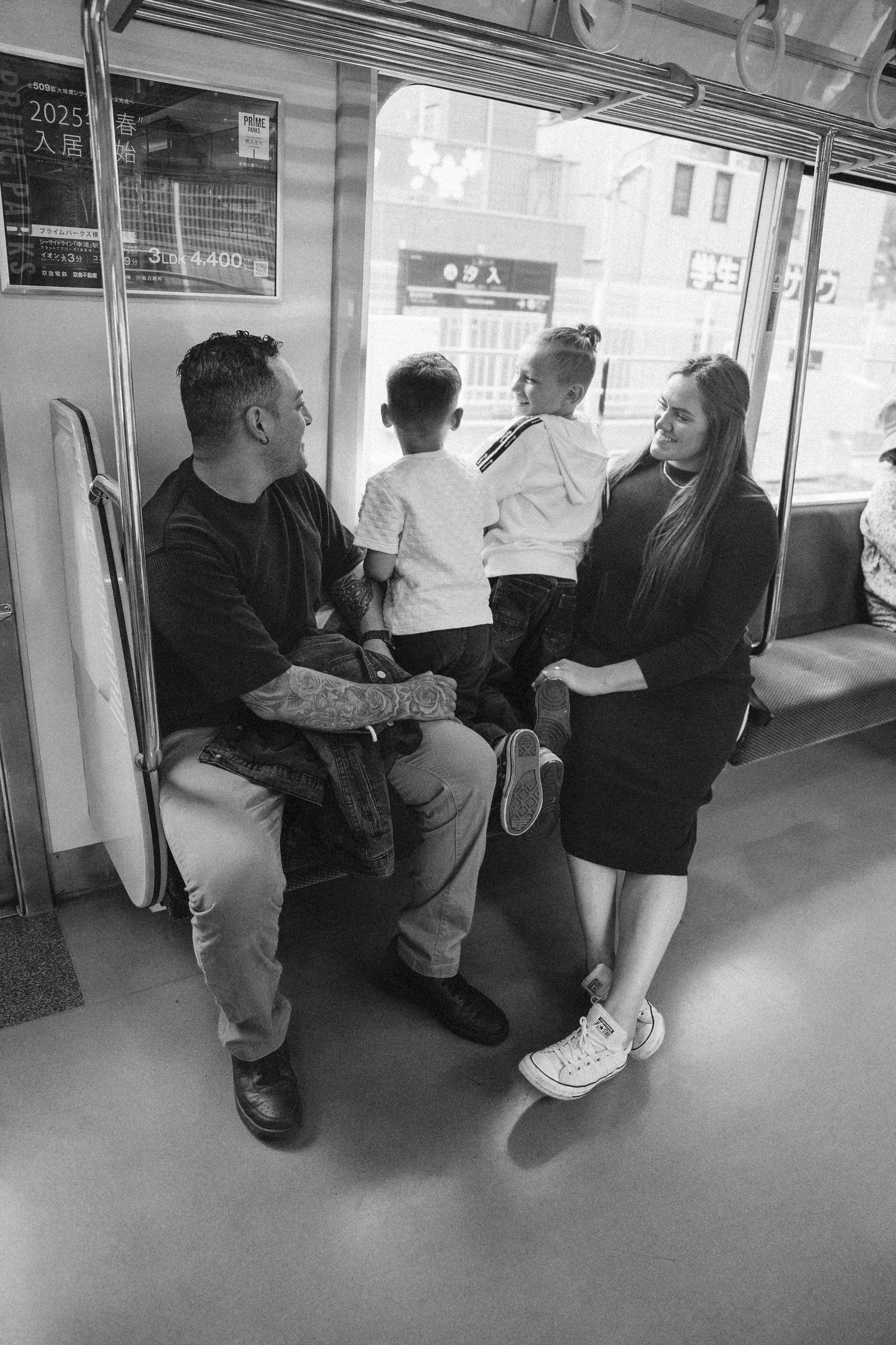 Passengers sitting inside a subway train car with grey flooring and white walls.