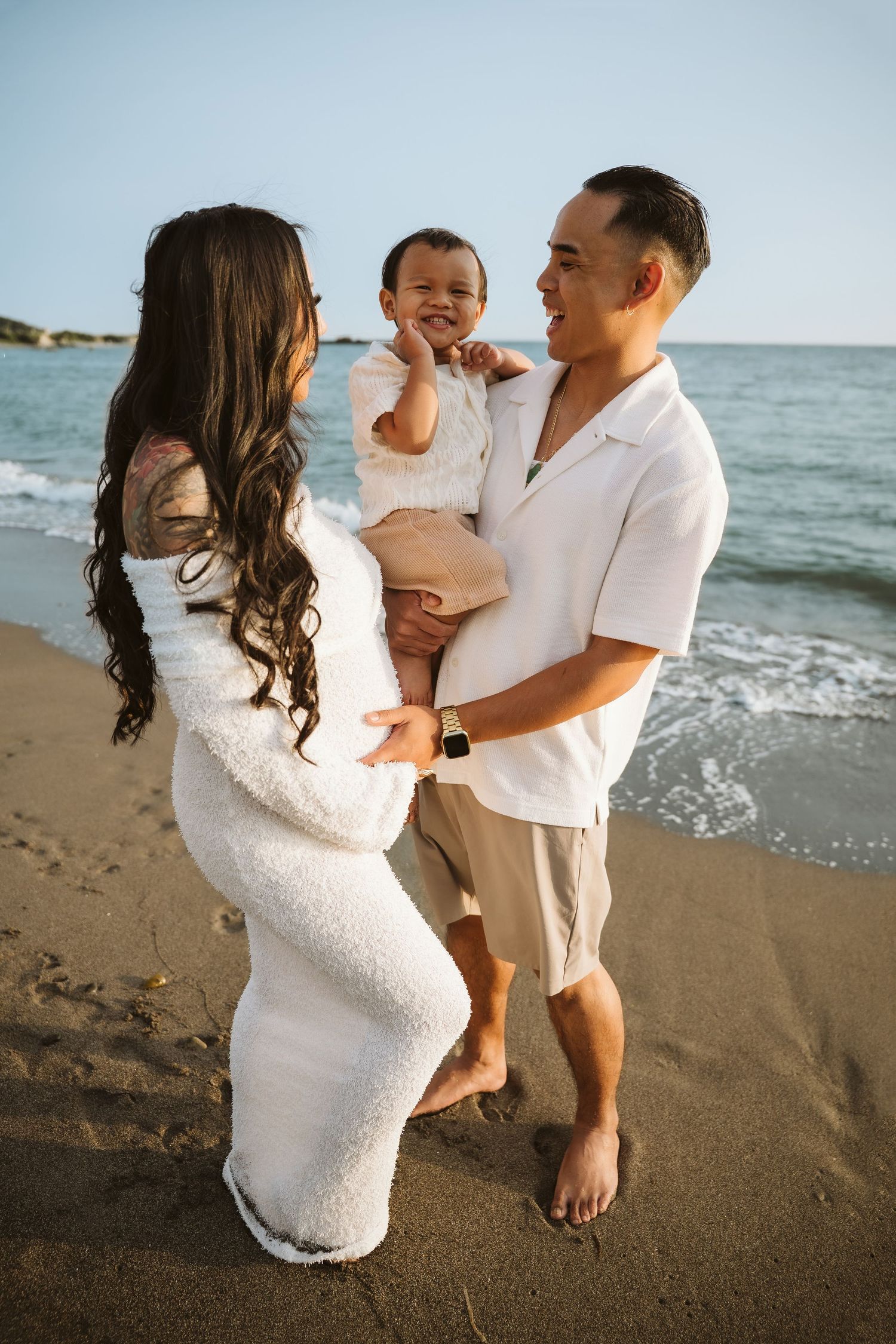 A family shares joyful moments together during a sunset photoshoot on a sandy beach by the ocean.