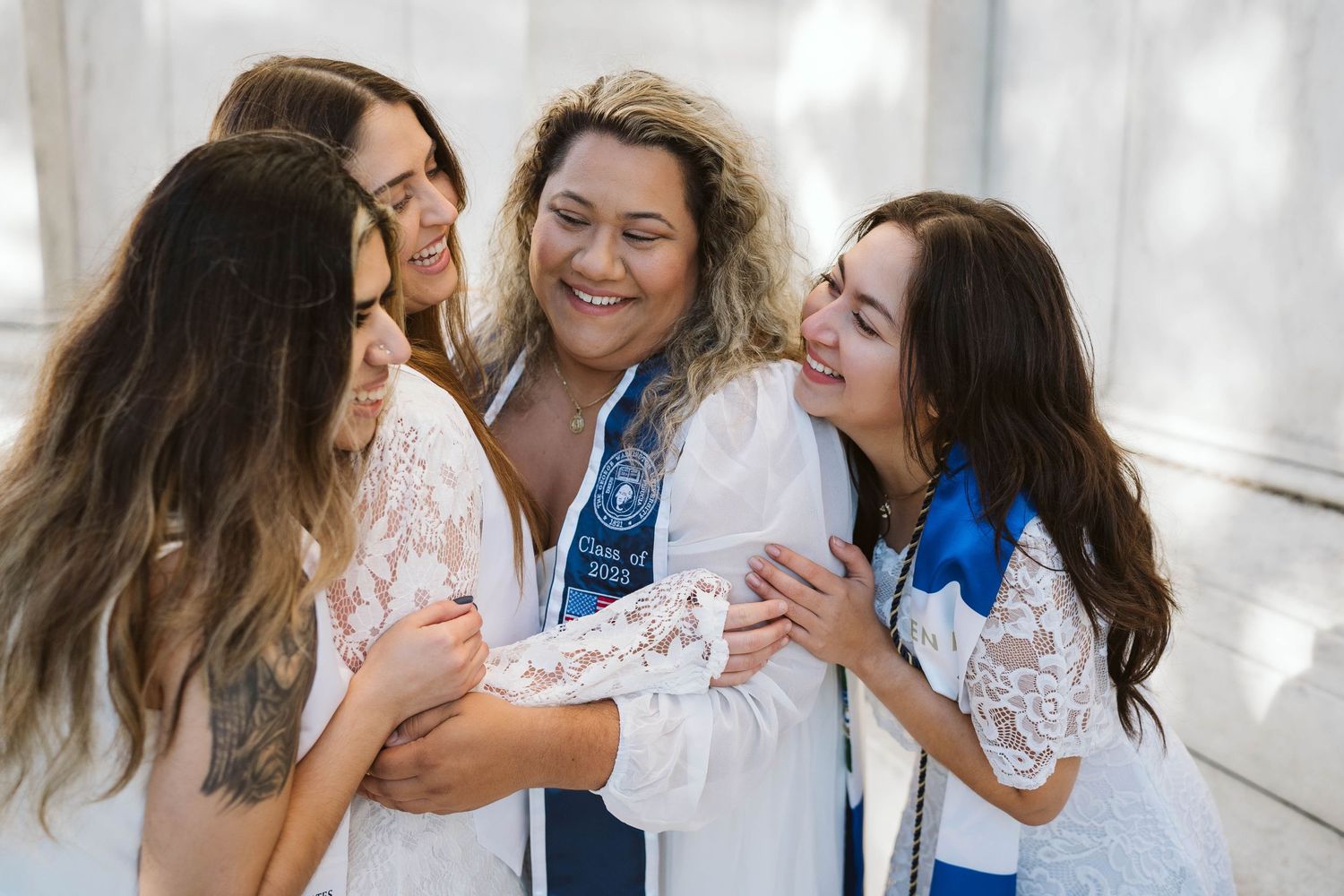 A group of friends wearing white lace and blue sharing a joyful laugh together in natural lighting.