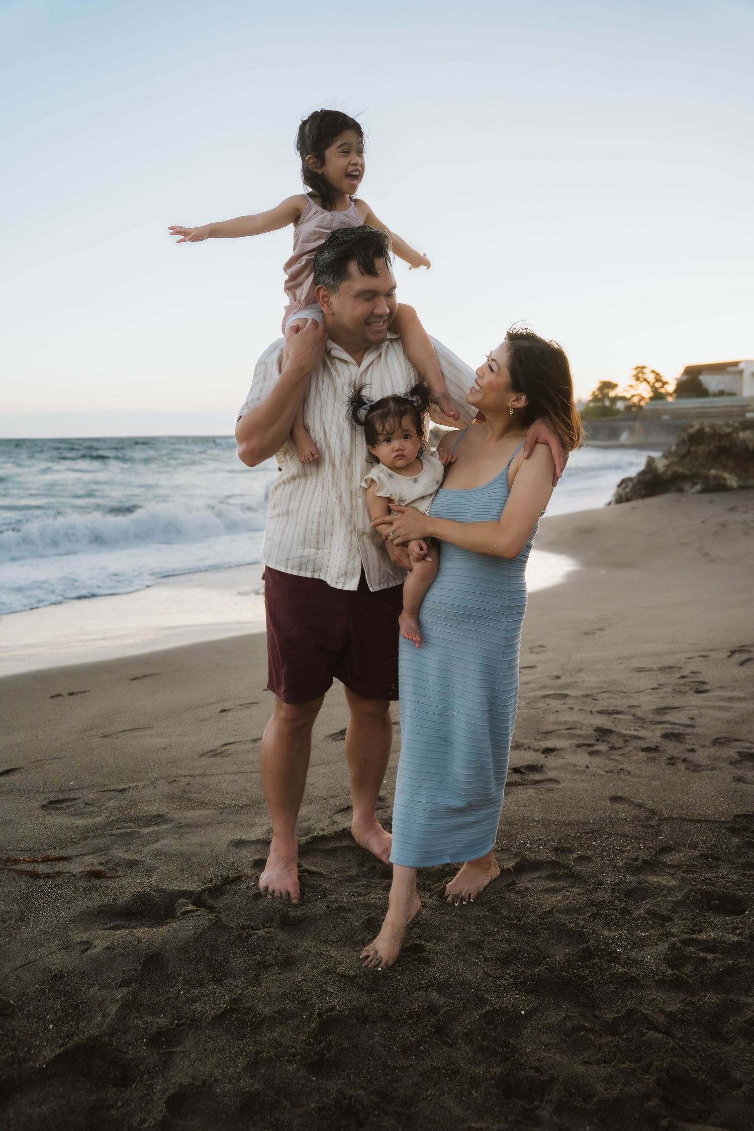 A family plays together on a black sand beach at sunset, sharing joyful moments near the ocean waves.