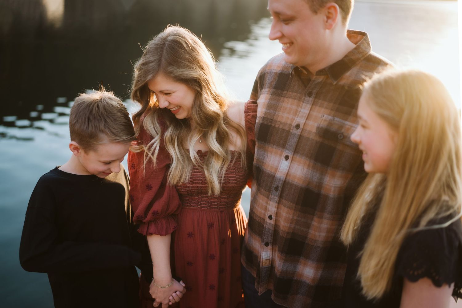 Four people stand together by a lake during golden hour, backlit by warm sunlight.