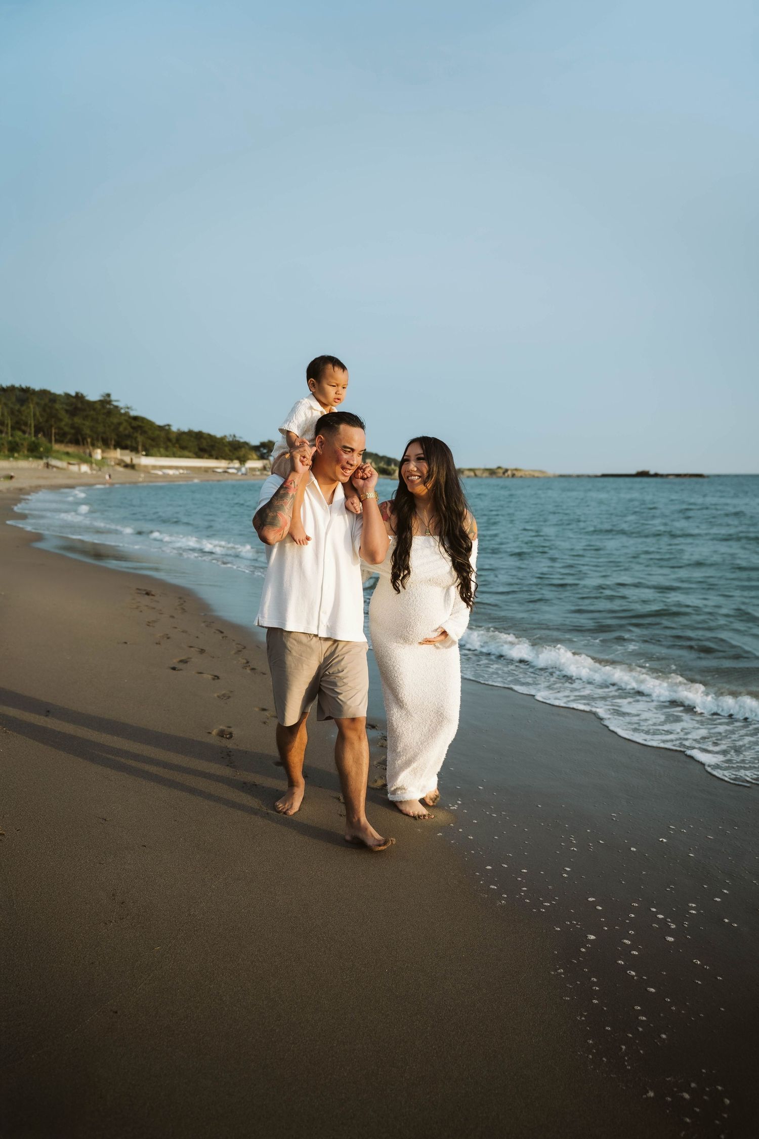 Family walks along scenic beach shoreline in matching white outfits at sunset.