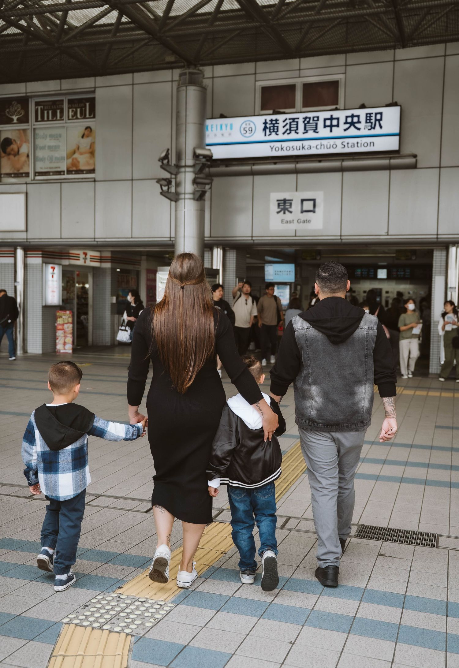 Commuters walking through a Japanese train station concourse with tactile paving and directional signs.