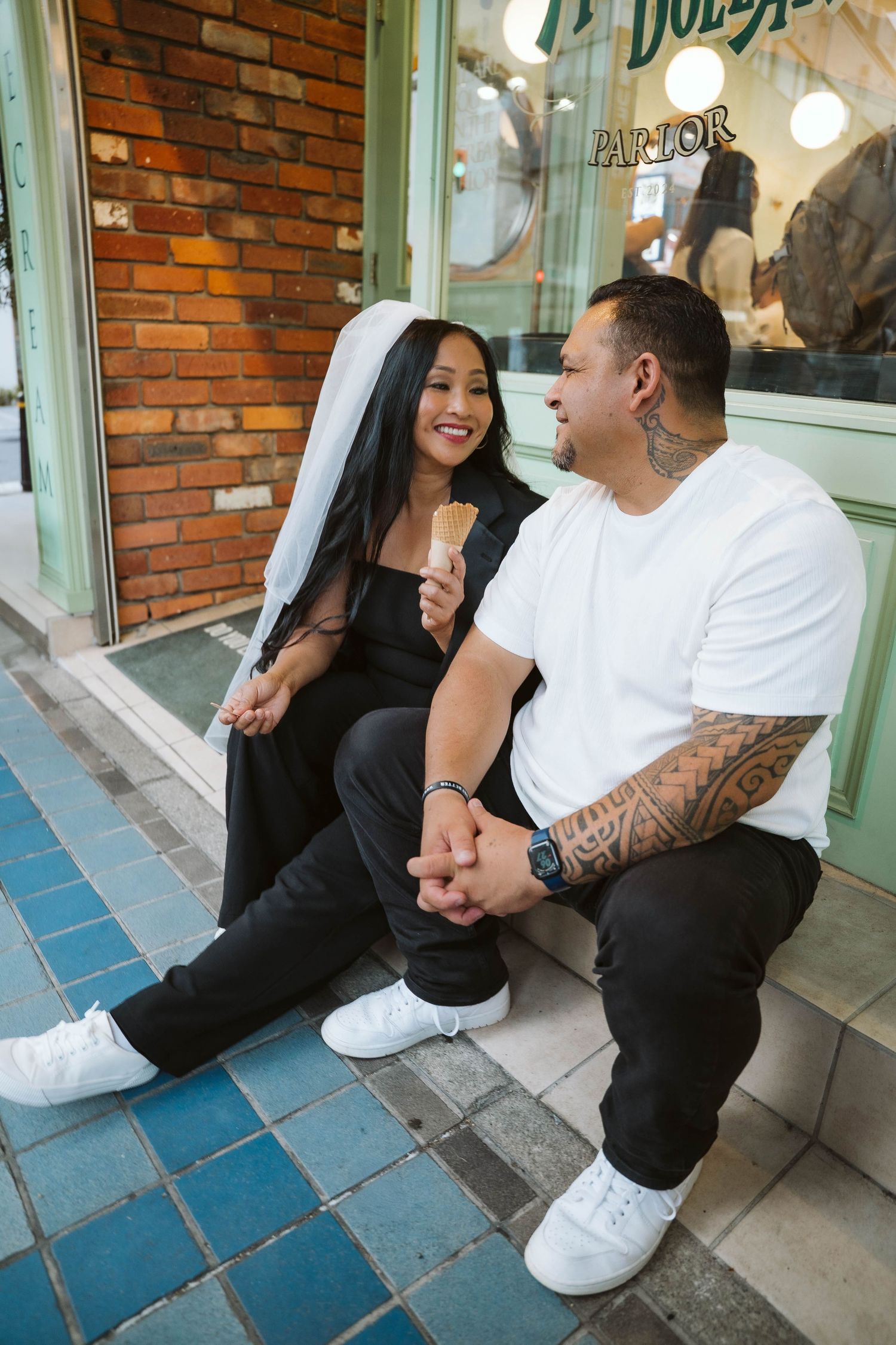 Couple sitting together on blue tiled steps against a brick wall storefront having a playful moment.