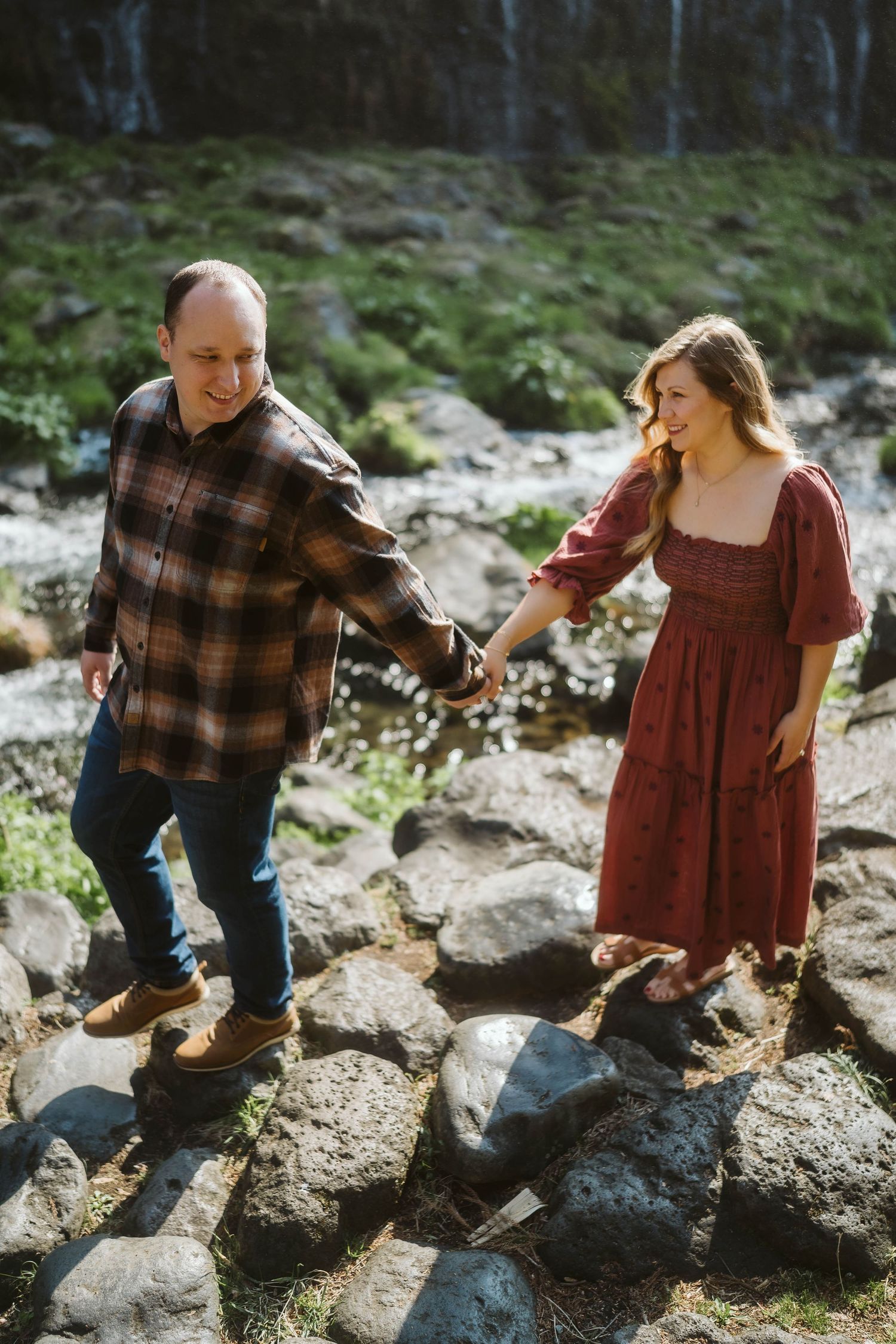 A couple sits together on rocky terrain while exploring outdoors in casual attire.
