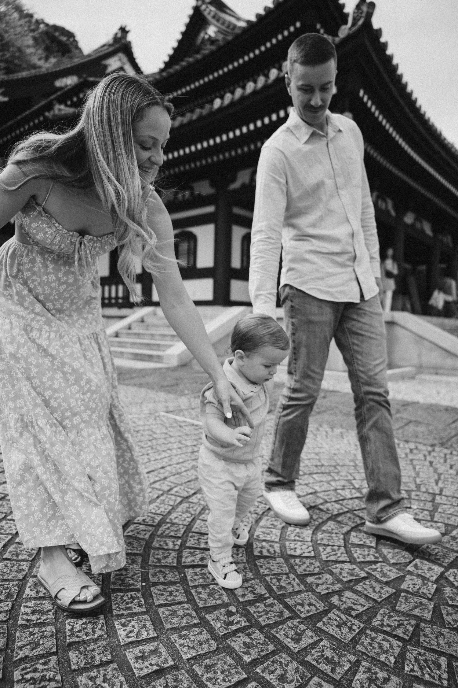 Family walking on decorative stone path at traditional Japanese temple in black and white.