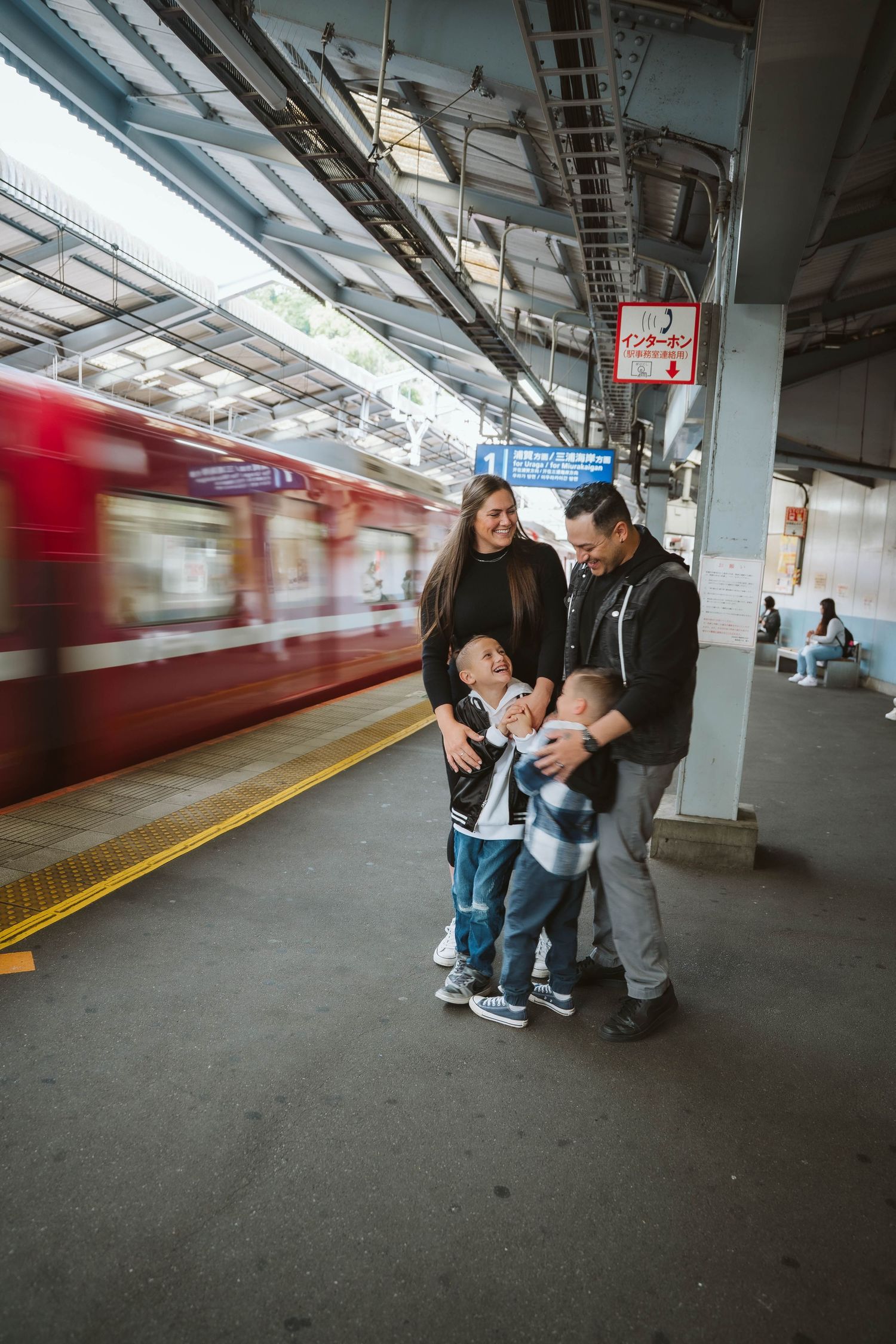 A group interacting on a train platform with blurred red train cars visible in the background.