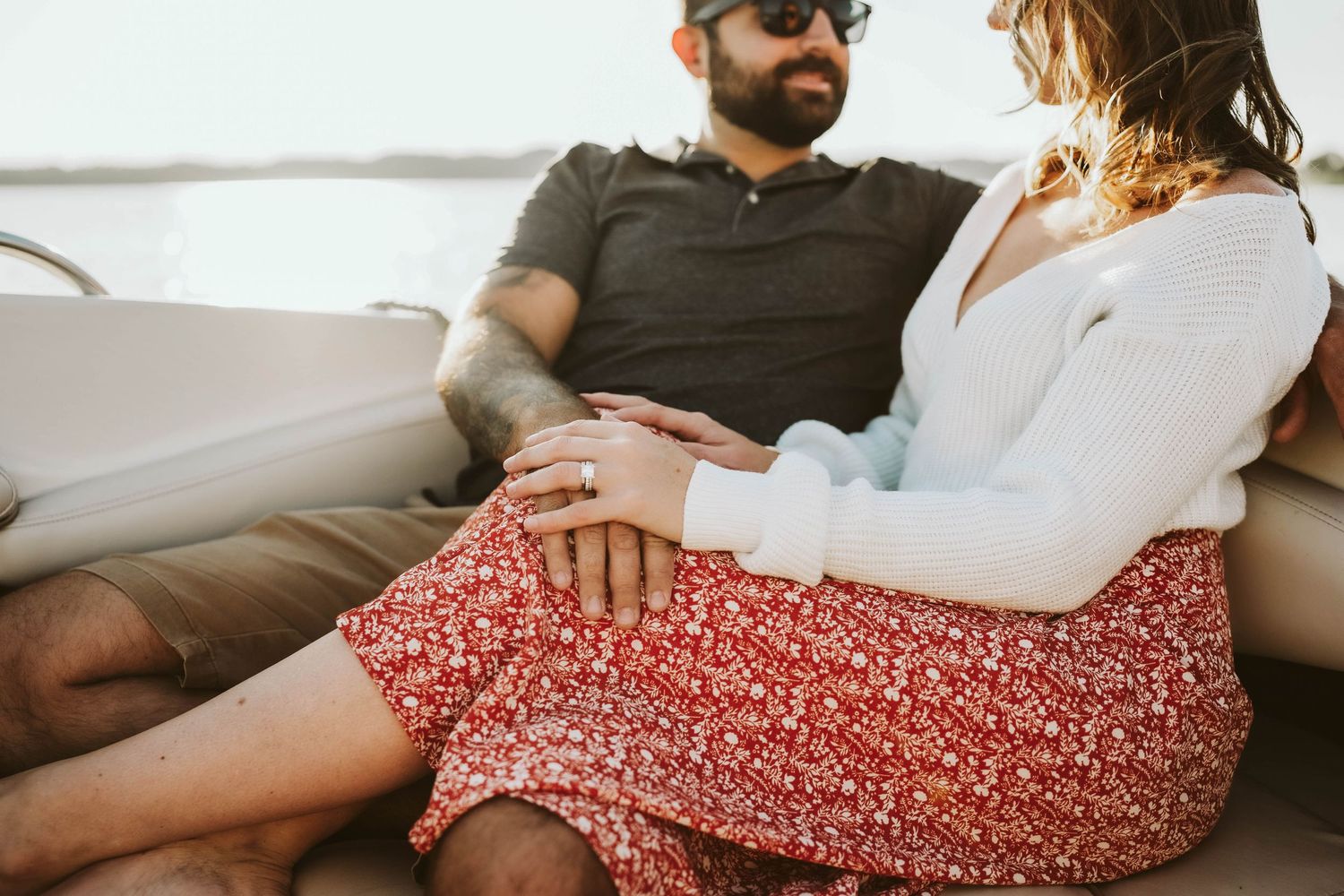 Close-up view of couple sitting together on couch with hands touching, wearing casual summer attire.