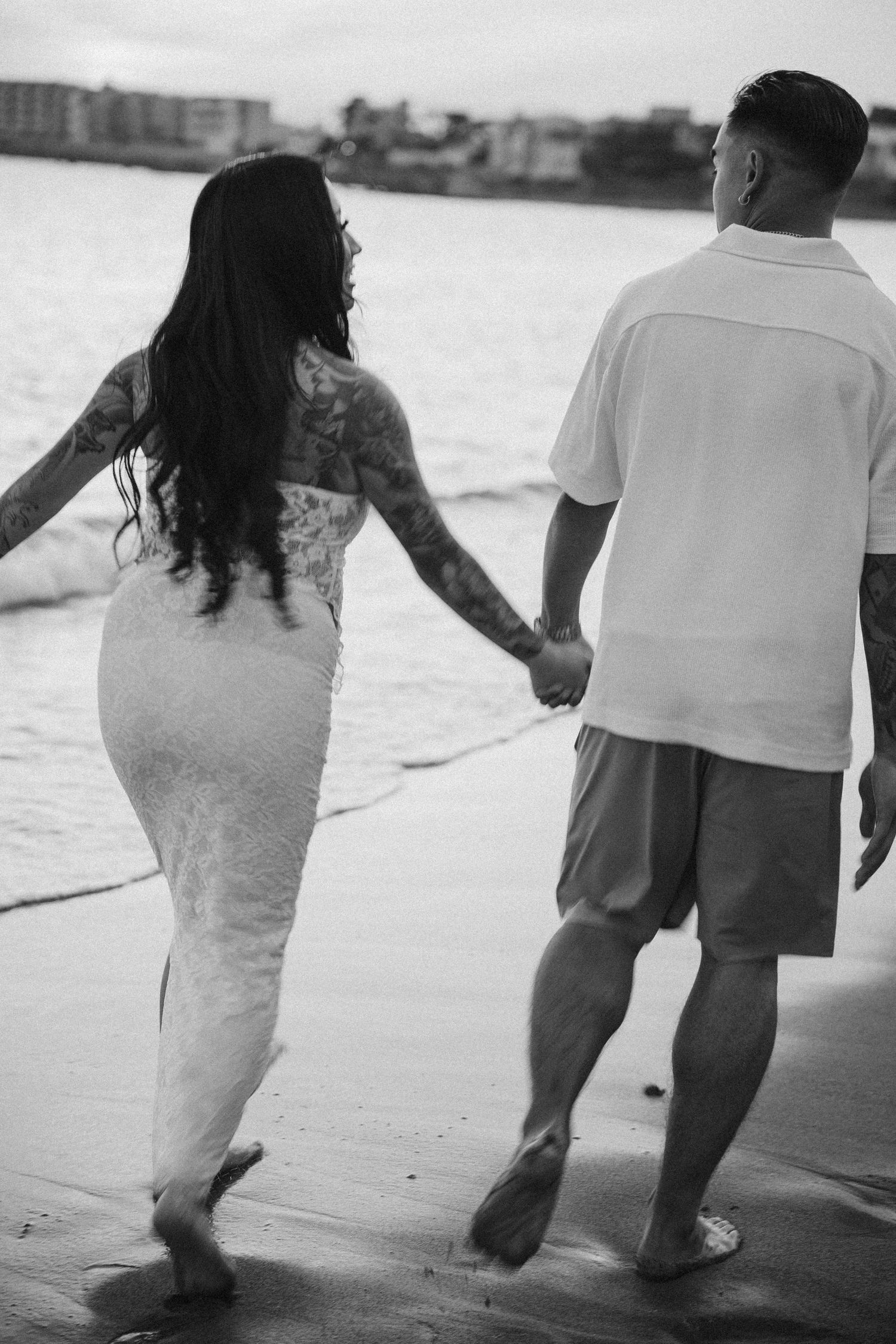 A couple walks together in black and white along a misty beach shoreline.