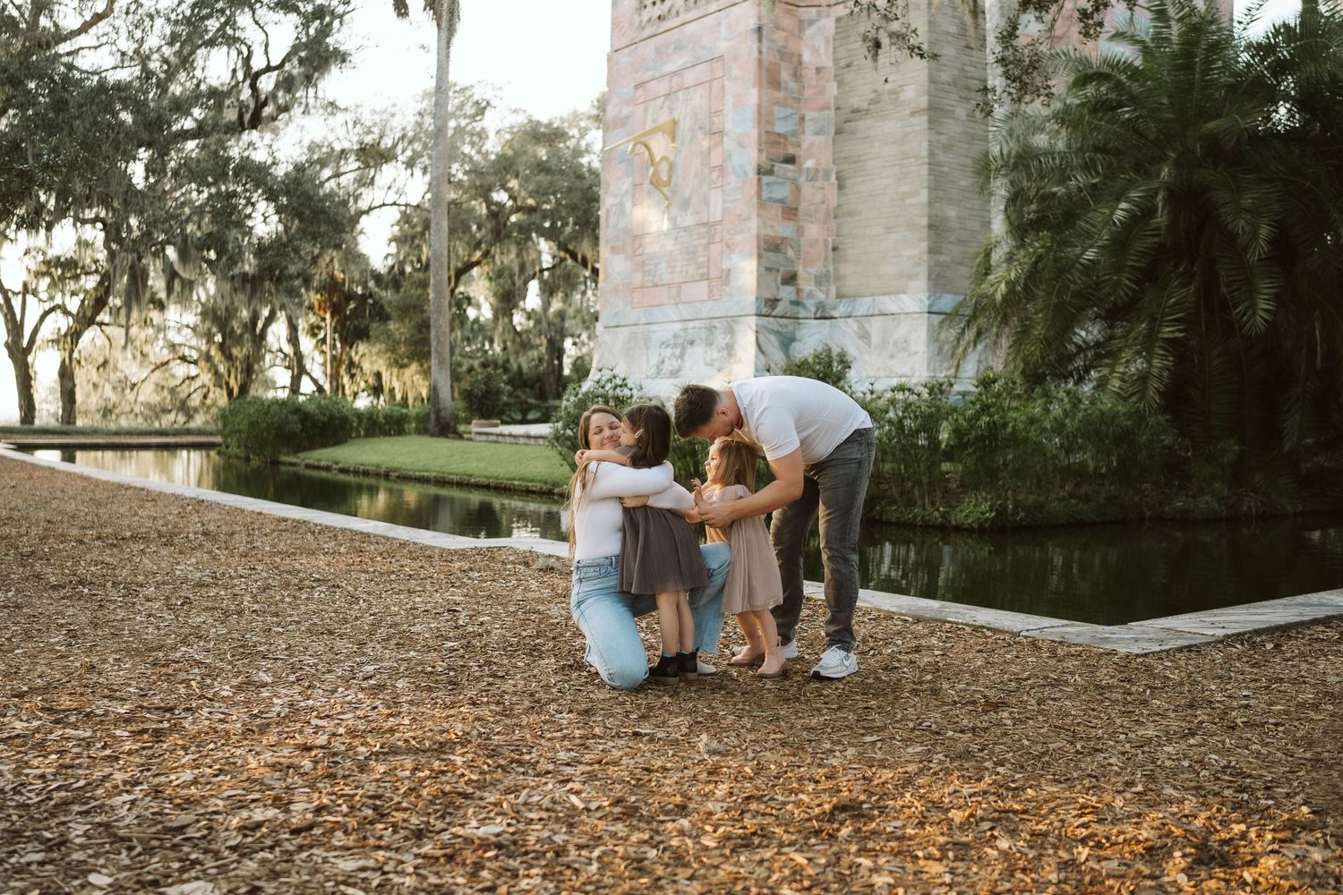 A family shares a loving moment together on a path covered in fallen leaves near a historic stone building.