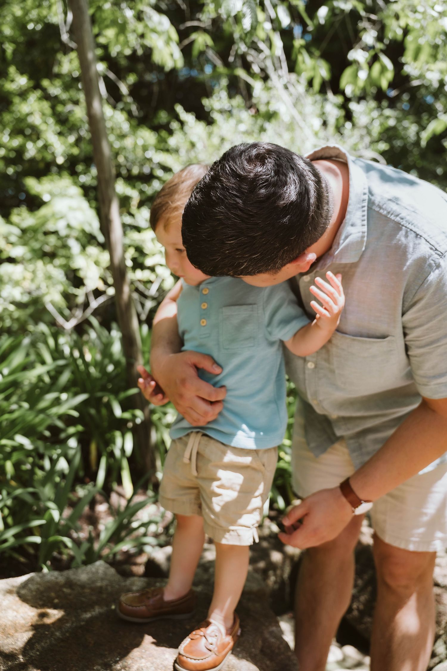 Parent and child explore nature together while bending down to examine something interesting on the ground.
