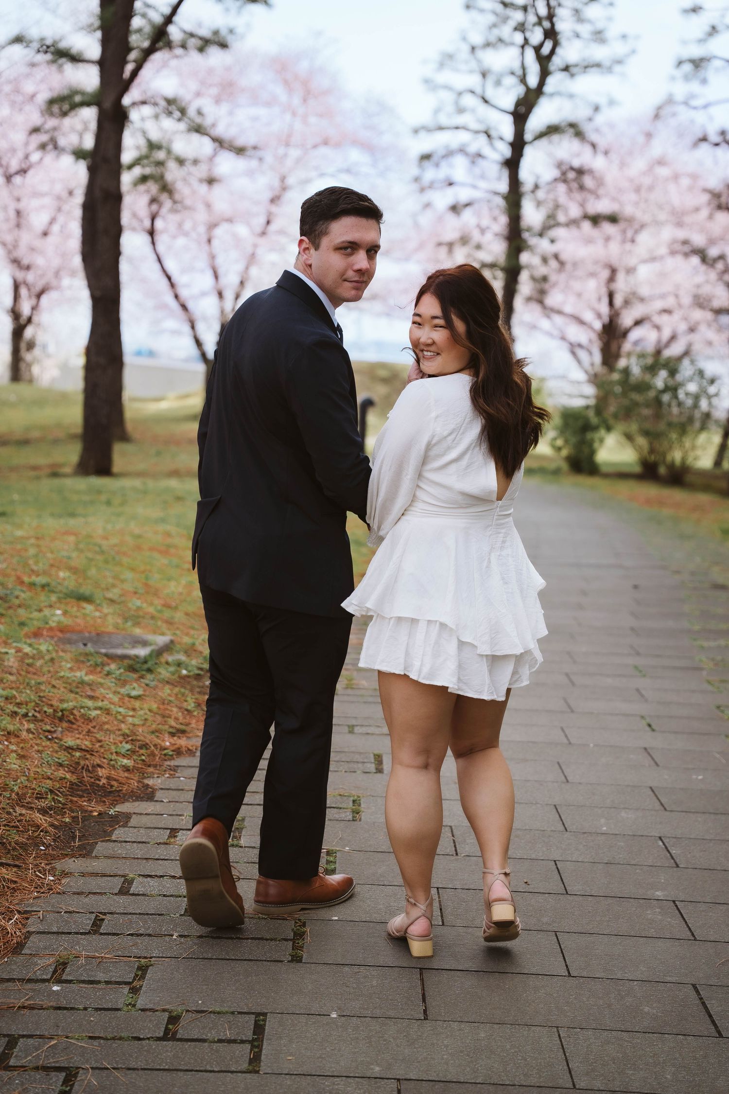 A couple walking along a path with blooming cherry blossom trees in the background during spring.