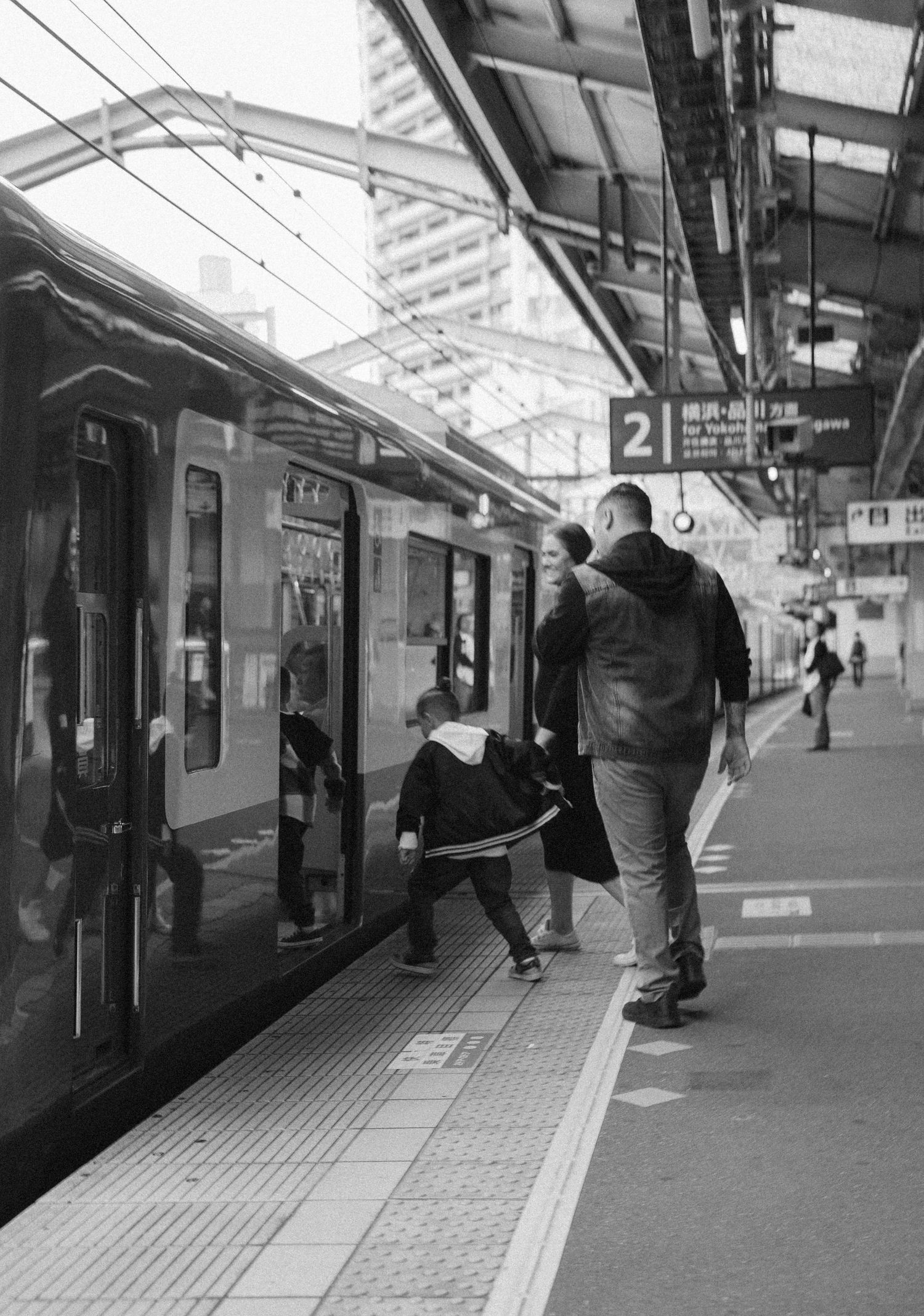 Passengers boarding a train at a Japanese railway platform with safety markings.