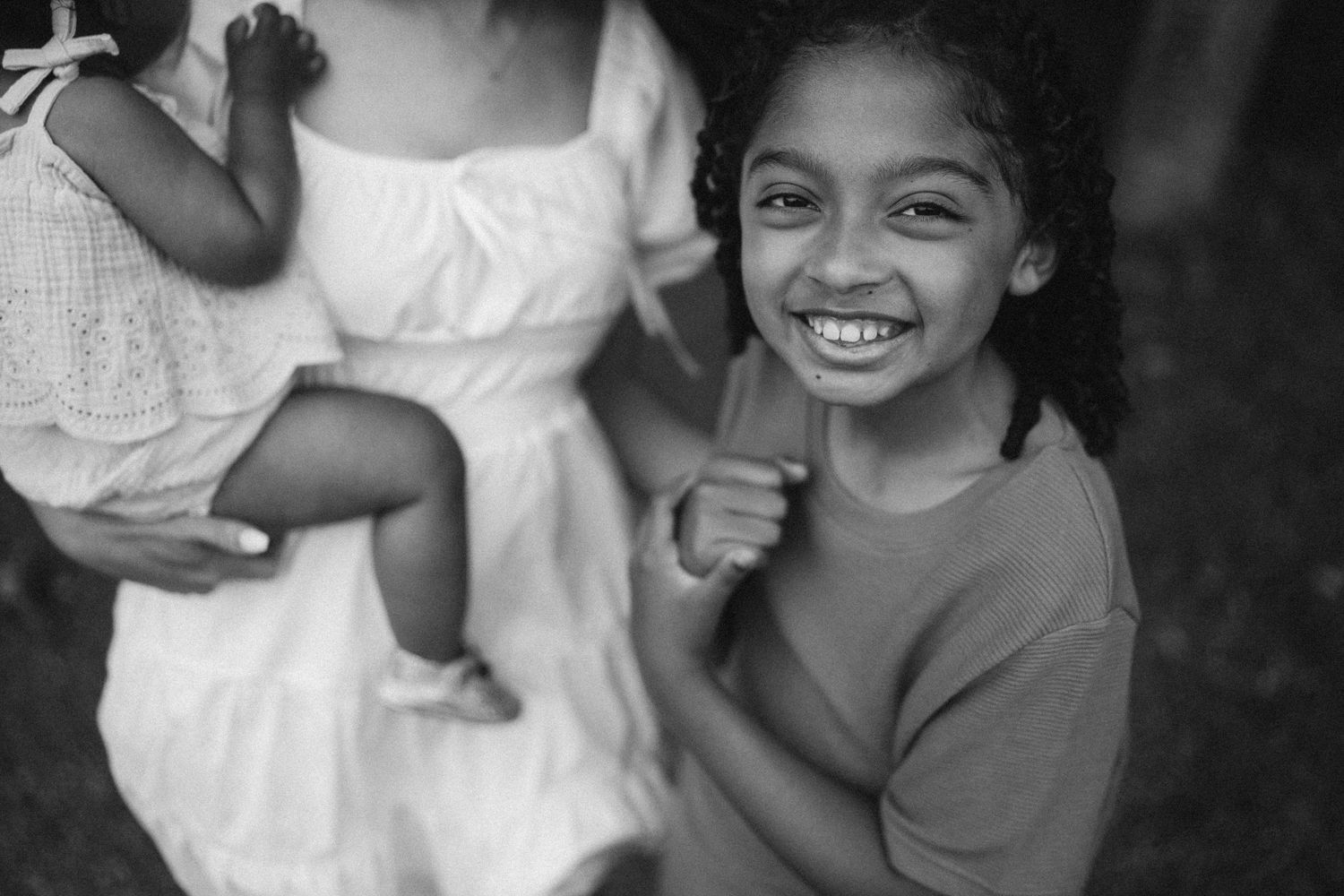 A young child in a dark sweater gives a bright smile in this black and white photograph.