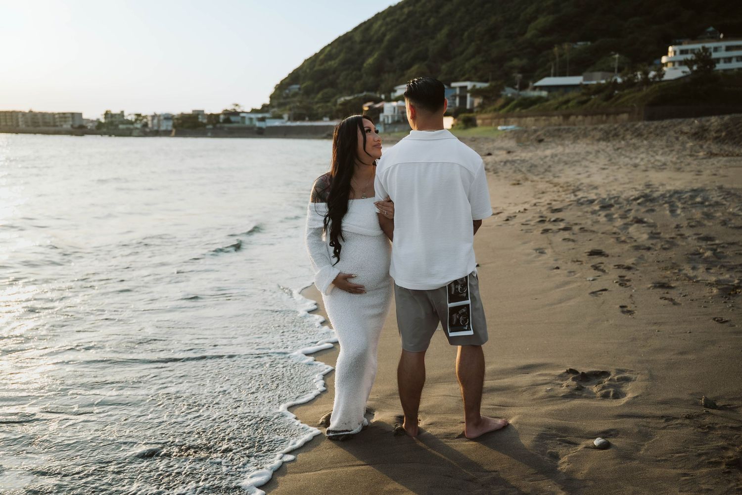 Couple walking along a scenic beach shoreline at sunset with waves crashing on the sand.