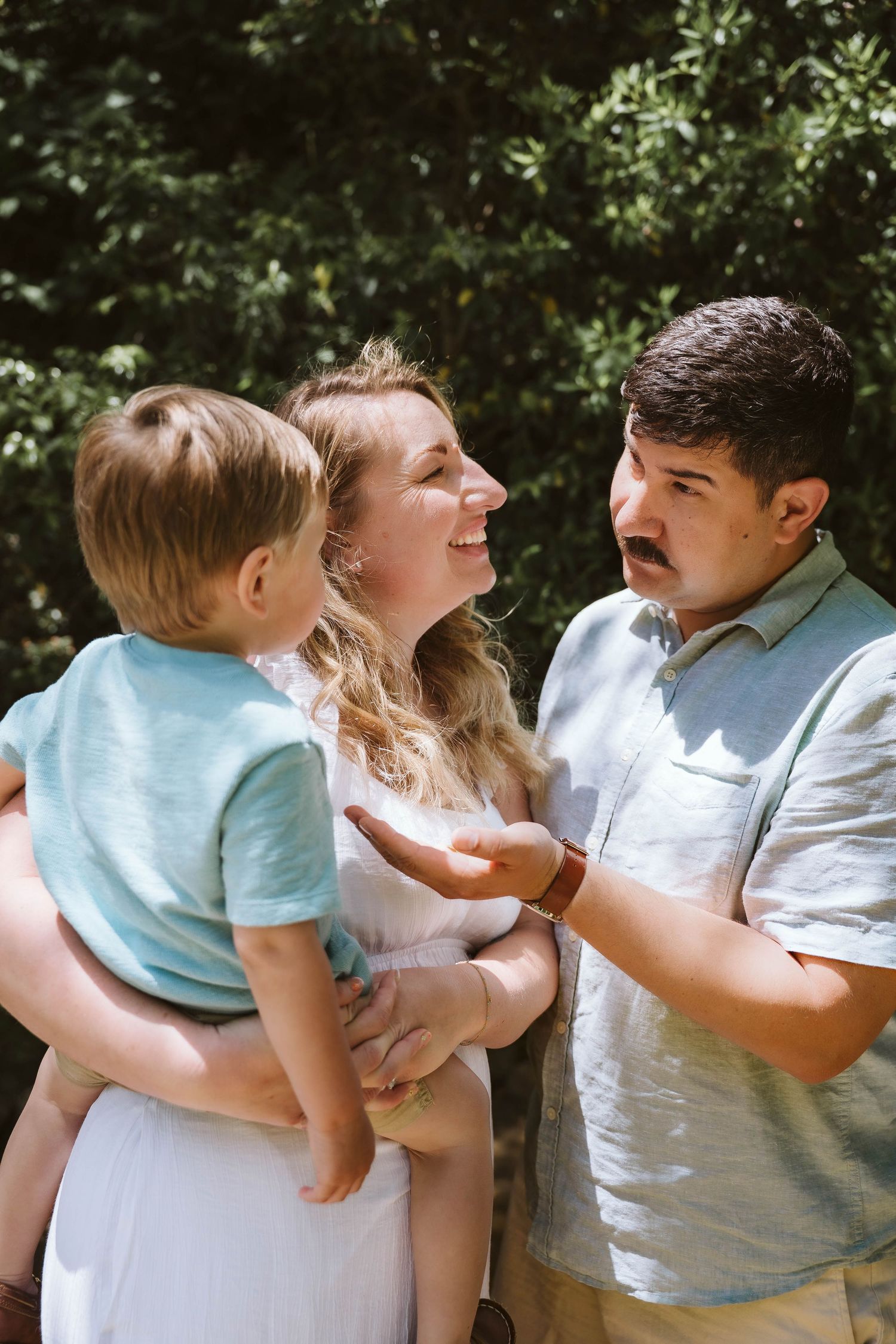 A sweet family moment captured in a series of embraces and kisses against a leafy outdoor backdrop.