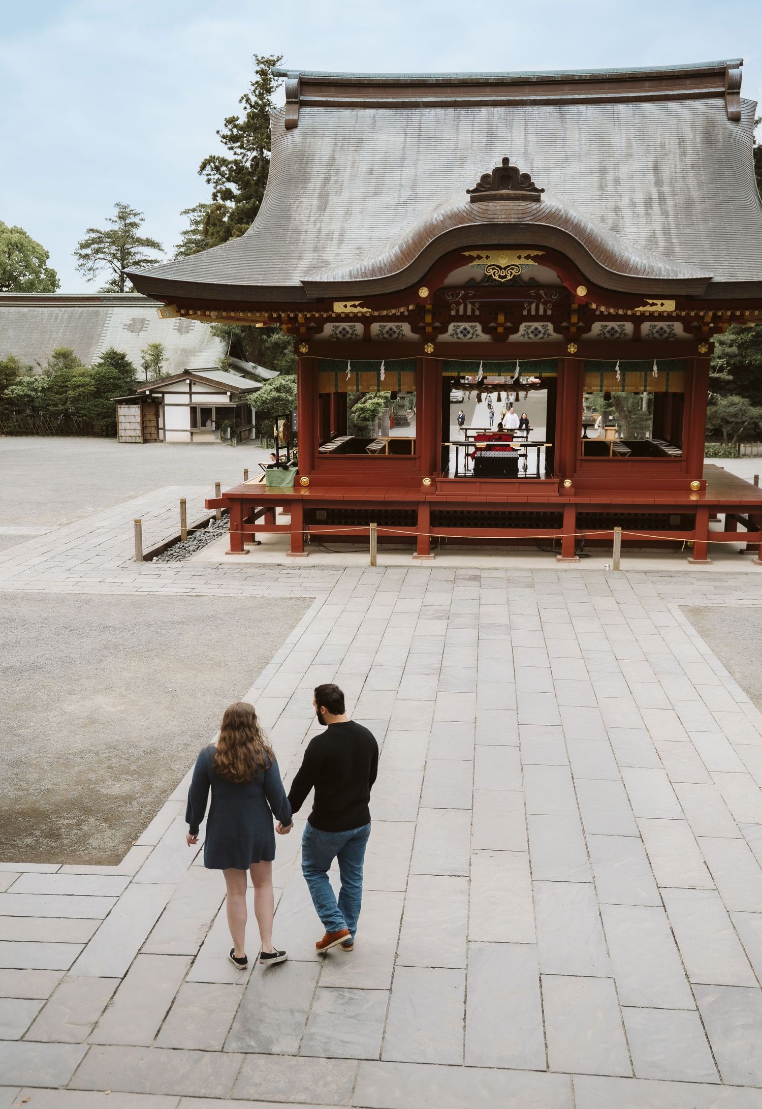 A couple walks hand in hand towards a traditional Japanese shrine building with ornate architecture.