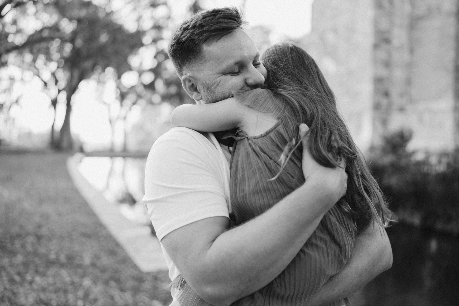 A black and white photo captures a romantic moment between two people embracing outdoors.