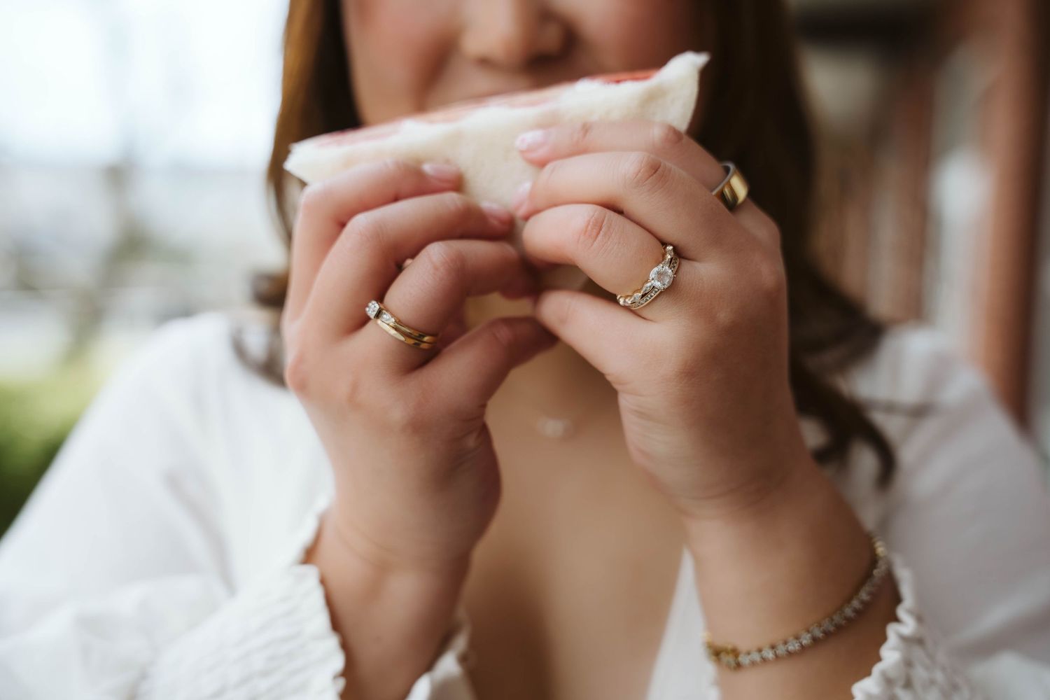 The image shows hands with delicate rings holding a soft tissue or napkin against a blurred background.