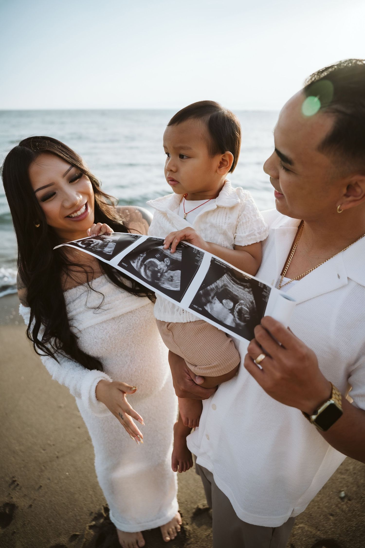 Family shares joyful moments looking at ultrasound photos together on a sunny beach.