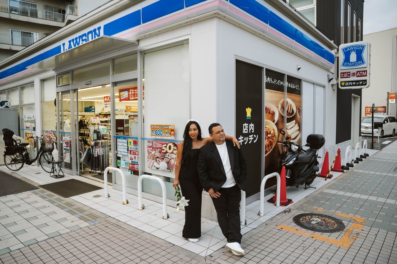 A stylish couple poses outside a Lawson convenience store in an urban Japanese setting.