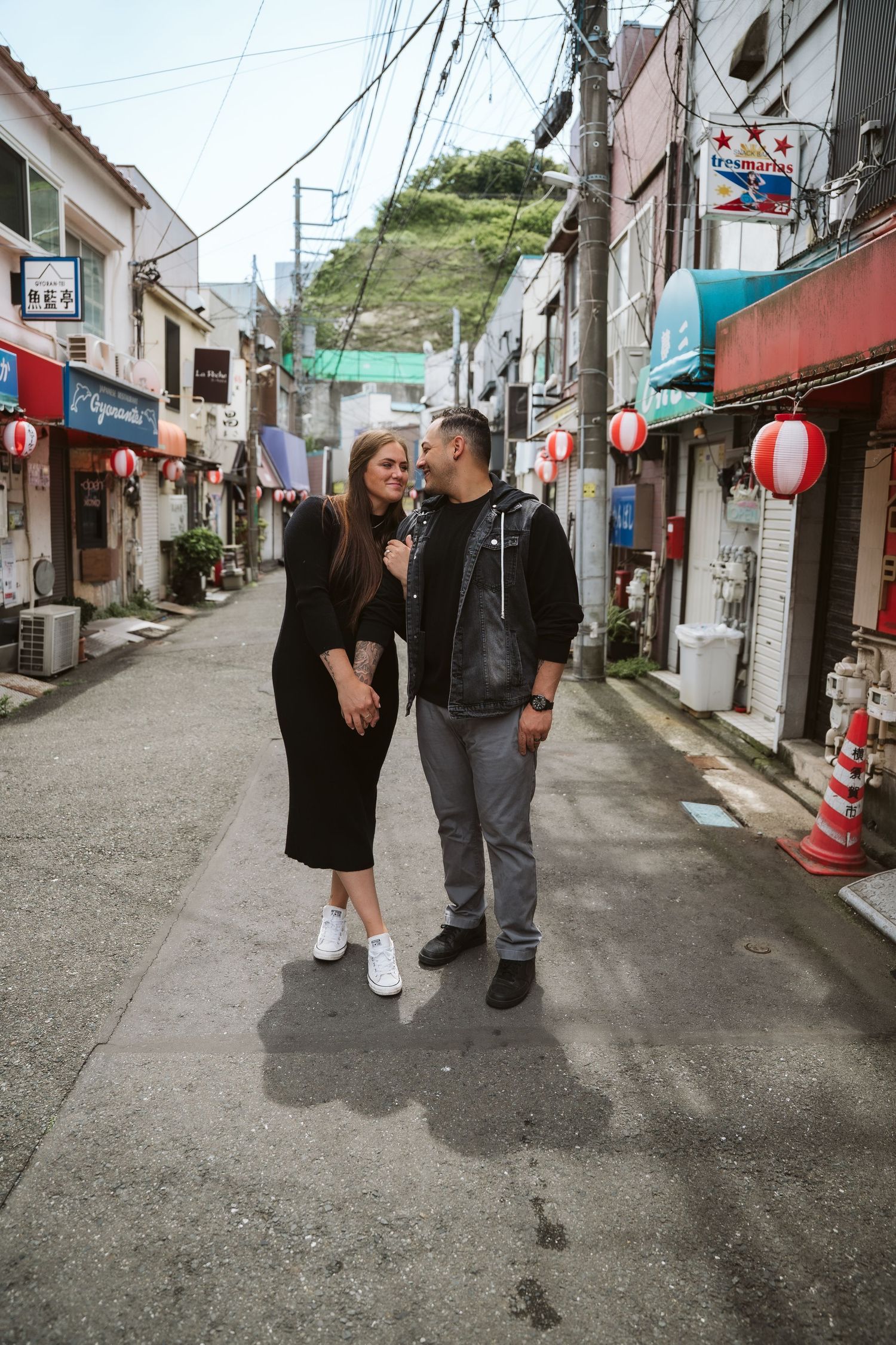 A couple walks together down a narrow alley lined with traditional Japanese lanterns and buildings.