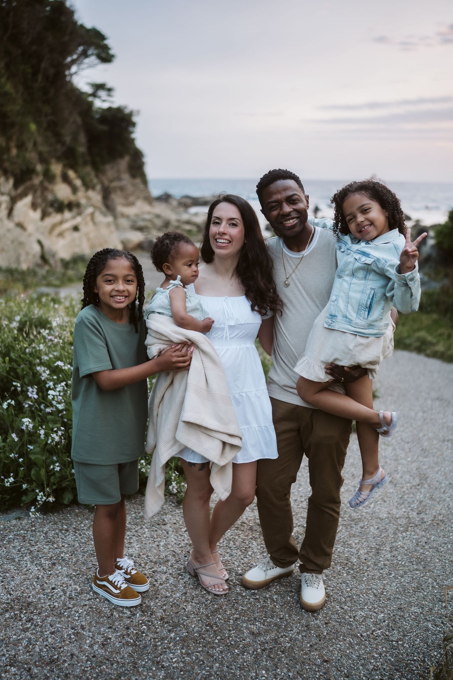 A family shares joyful moments together on a scenic coastal path during a casual outdoor photoshoot.