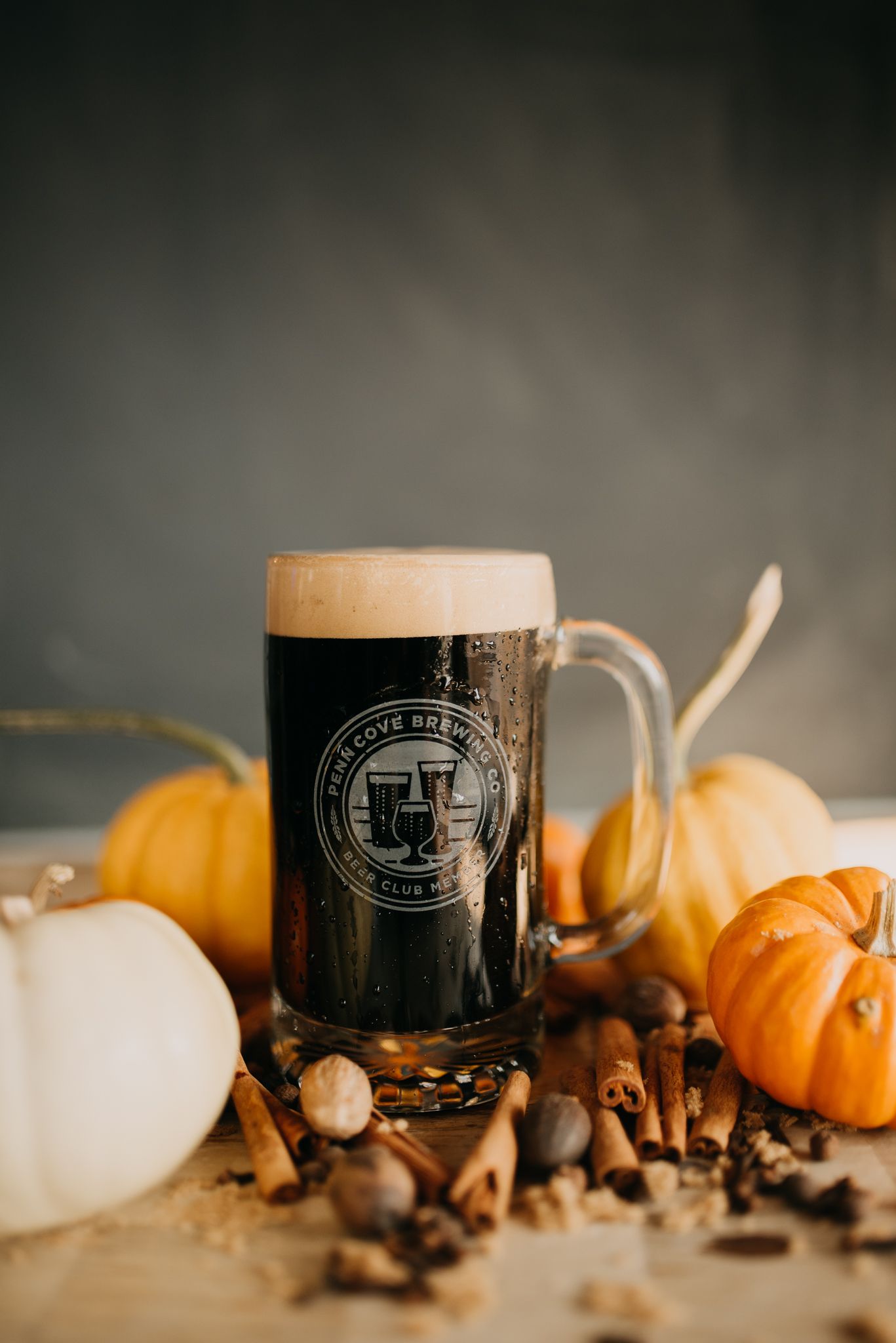 Dark stout beer in branded glass mug surrounded by pumpkins and autumn spices on table.